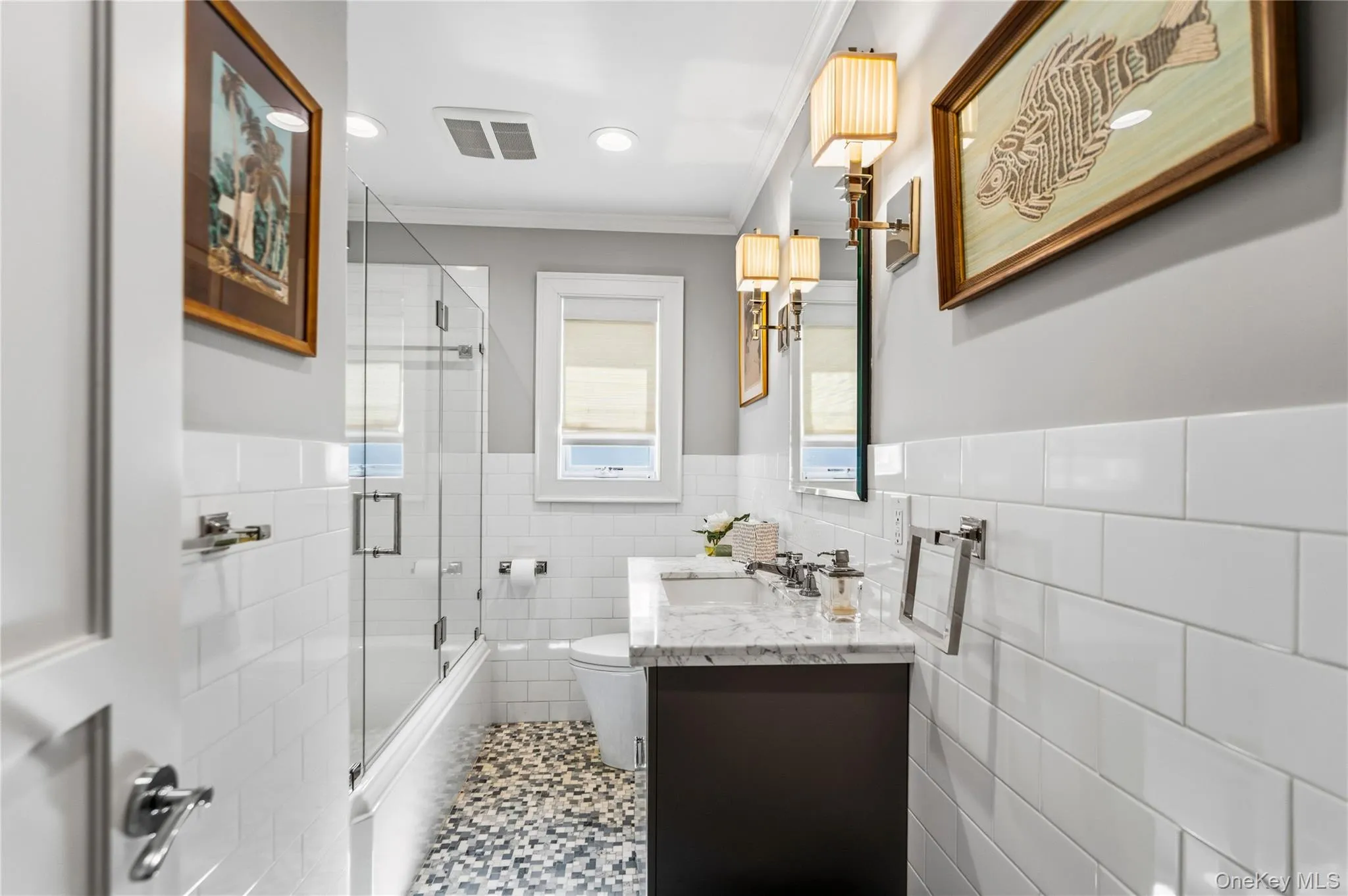 Bathroom featuring white subway tile wall cladding, a Marable countertop vanity with an undermount sink, a shower enclosure with a glass door, and patterned mosaic tile flooring Bathroom featuring white subway tile wall cladding, a Marable countertop vanity with an undermount sink, a shower enclosure with a glass door, and patterned mosaic tile flooring
