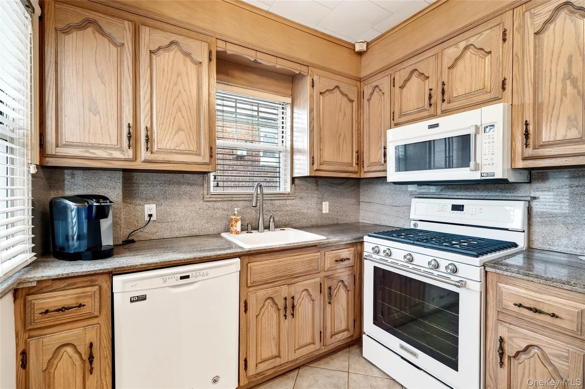 Kitchen featuring white appliances, tasteful backsplash, light tile patterned floors, and light stone counters Kitchen featuring white appliances, tasteful backsplash, light tile patterned floors, and light stone counters