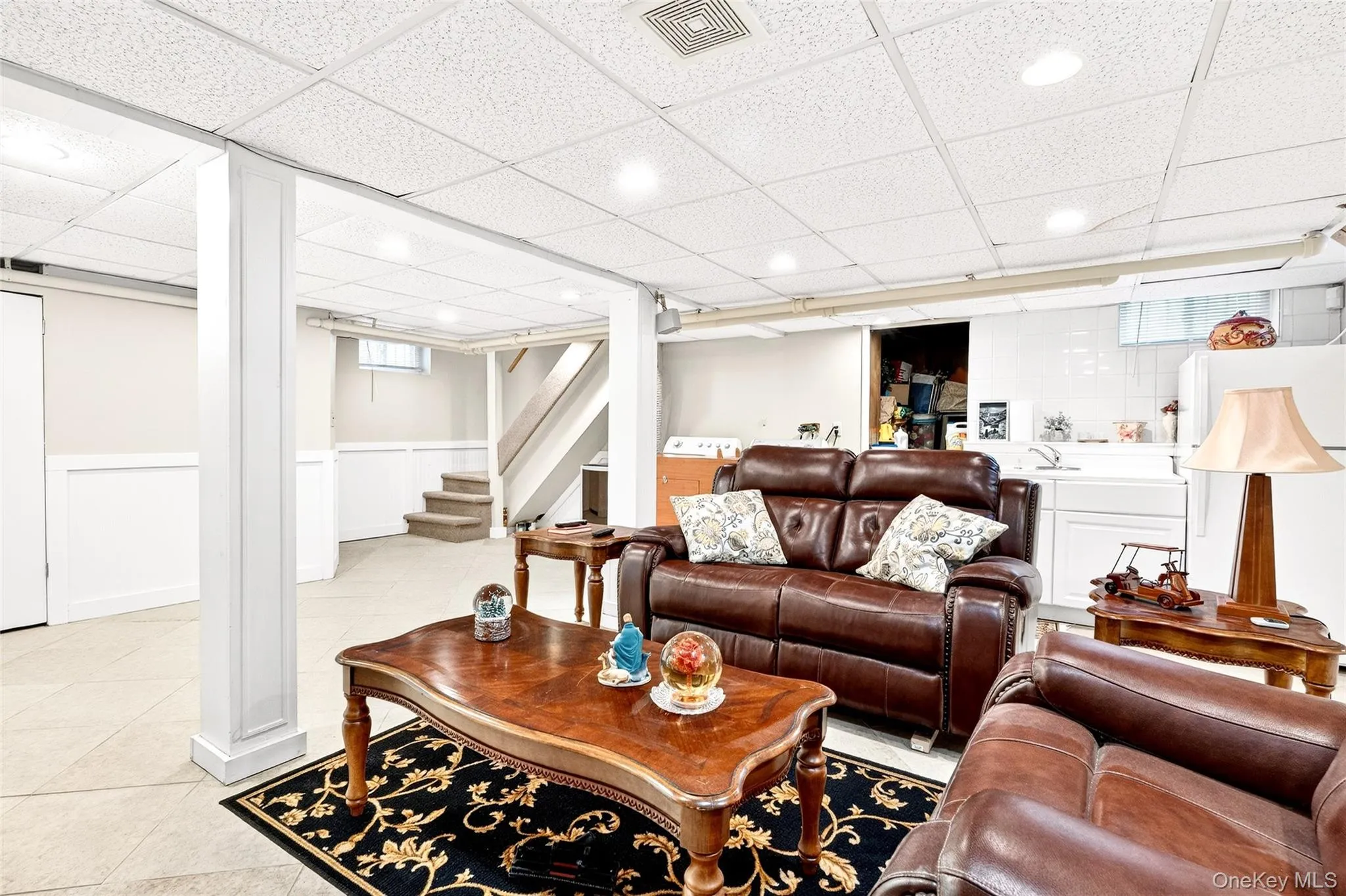 Living area with a paneled ceiling, light tile patterned flooring, stairs, and wainscoting Living area with a paneled ceiling, light tile patterned flooring, stairs, and wainscoting