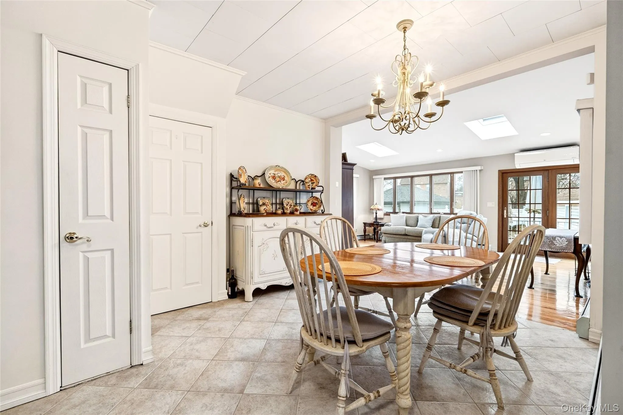 Dining room with crown molding, a chandelier, french doors, light tile patterned floors, and a skylight Dining room with crown molding, a chandelier, french doors, light tile patterned floors, and a skylight