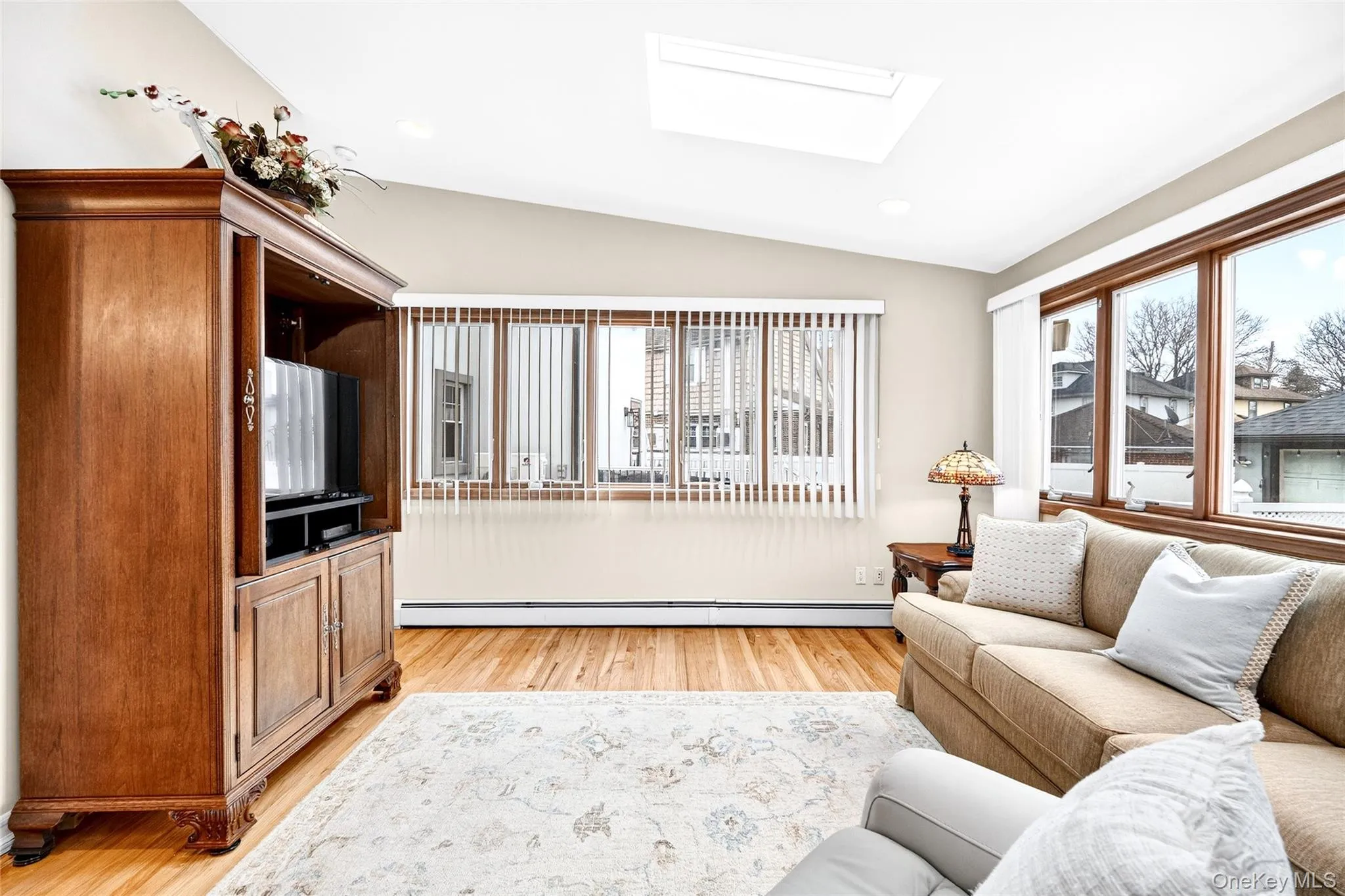 Living room featuring vaulted ceiling, light wood-type flooring, a skylight, a baseboard heating unit, and recessed lighting Living room featuring vaulted ceiling, light wood-type flooring, a skylight, a baseboard heating unit, and recessed lighting
