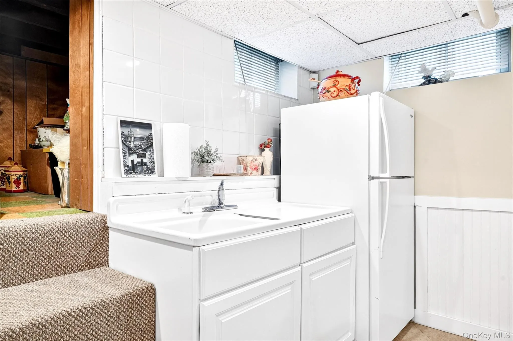 Kitchen with freestanding refrigerator, a wainscoted wall, a drop ceiling, white cabinets, and light countertops Kitchen with freestanding refrigerator, a wainscoted wall, a drop ceiling, white cabinets, and light countertops