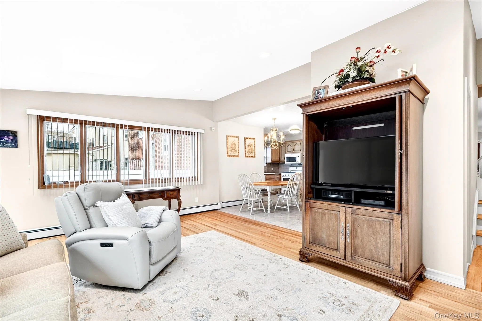 Living room featuring vaulted ceiling, a chandelier, light wood-type flooring, a baseboard heating unit, and a baseboard radiator Living room featuring vaulted ceiling, a chandelier, light wood-type flooring, a baseboard heating unit, and a baseboard radiator