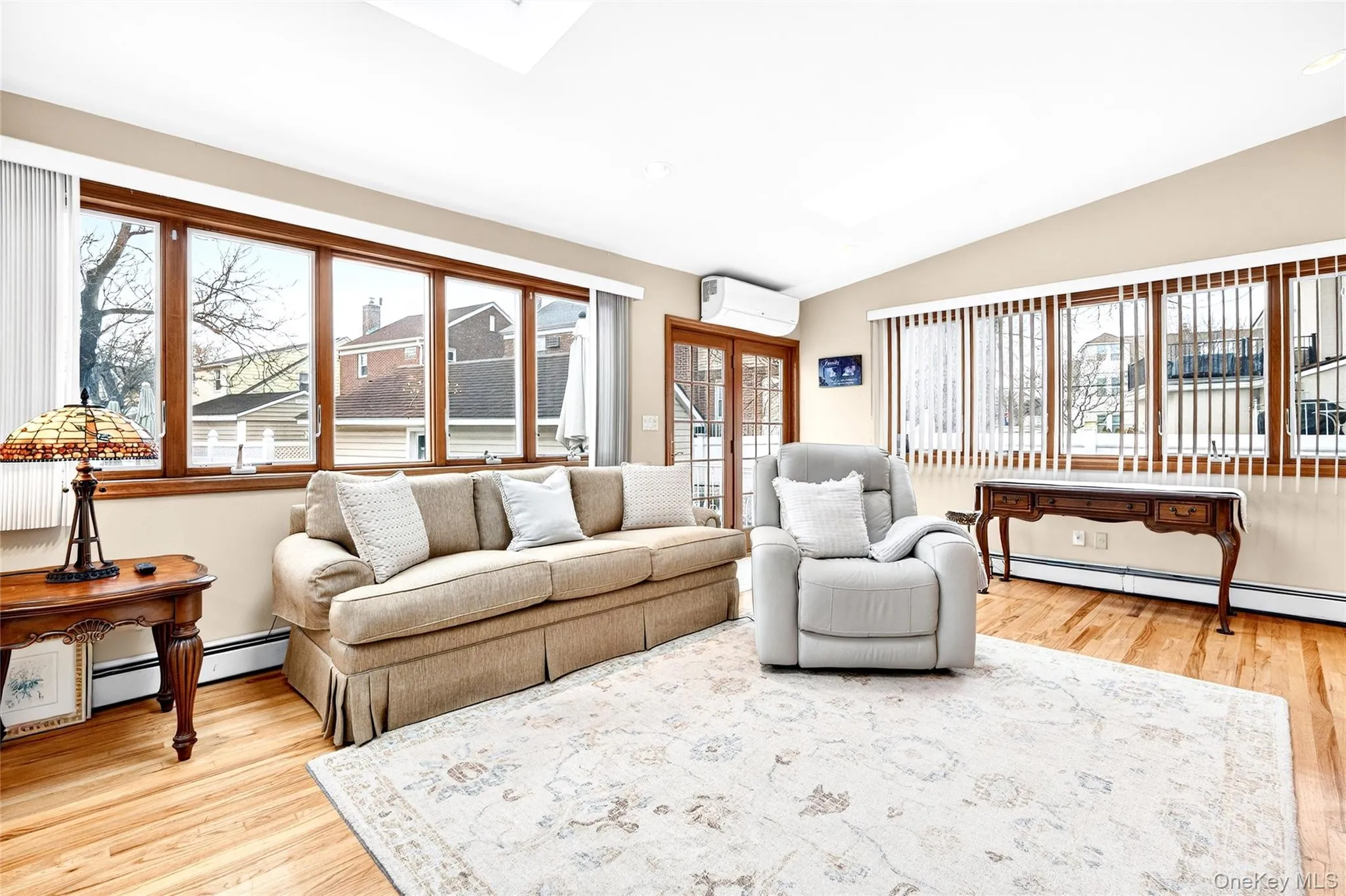 Living room featuring lofted ceiling, light wood-style floors, healthy amount of natural light, and a wall mounted AC Living room featuring lofted ceiling, light wood-style floors, healthy amount of natural light, and a wall mounted AC