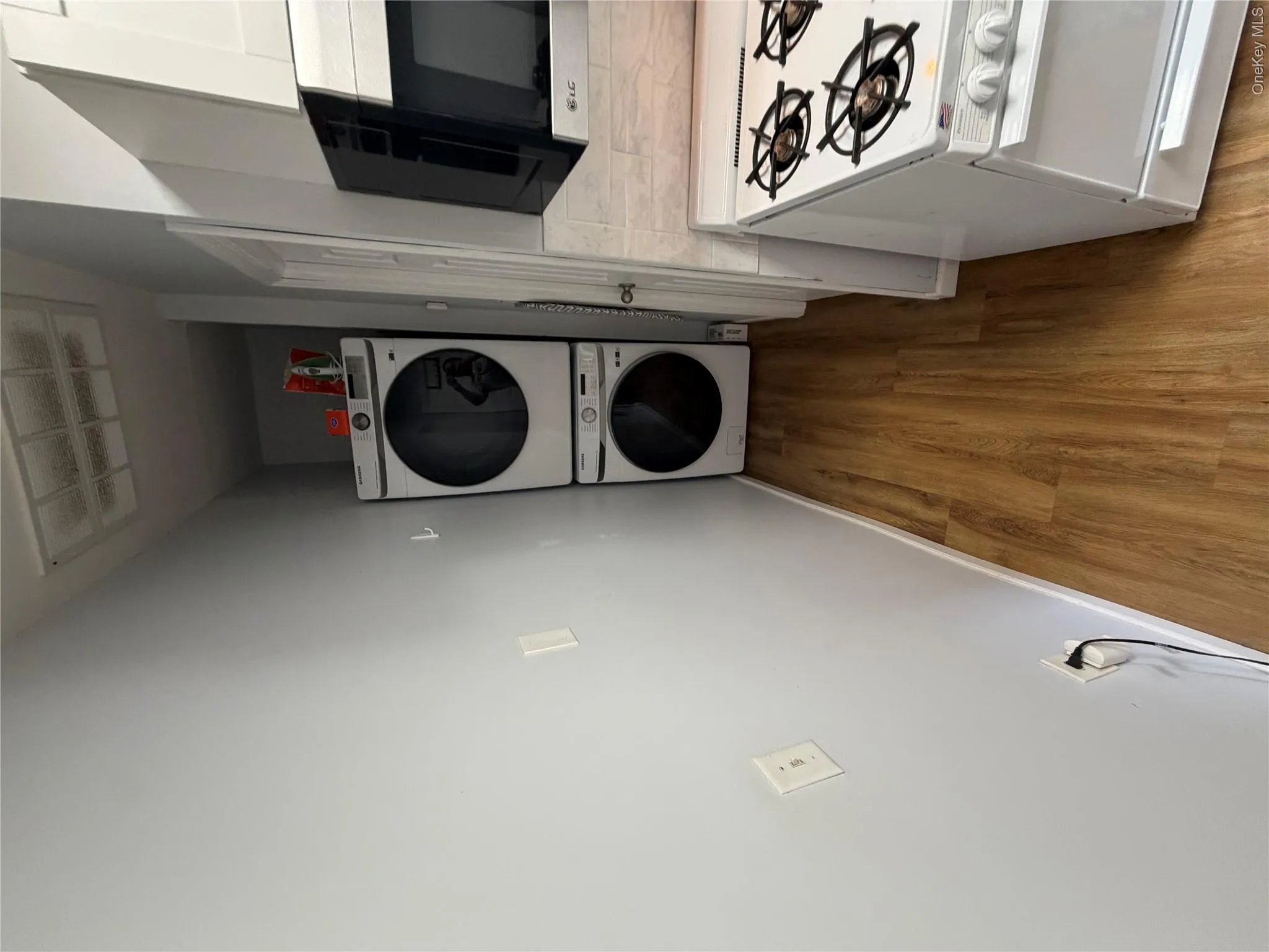 Stackable washer and dryer, wood-finish flooring, white wall paint, wall-mounted exhaust hood, and white gas range Stackable washer and dryer, wood-finish flooring, white wall paint, wall-mounted exhaust hood, and white gas range