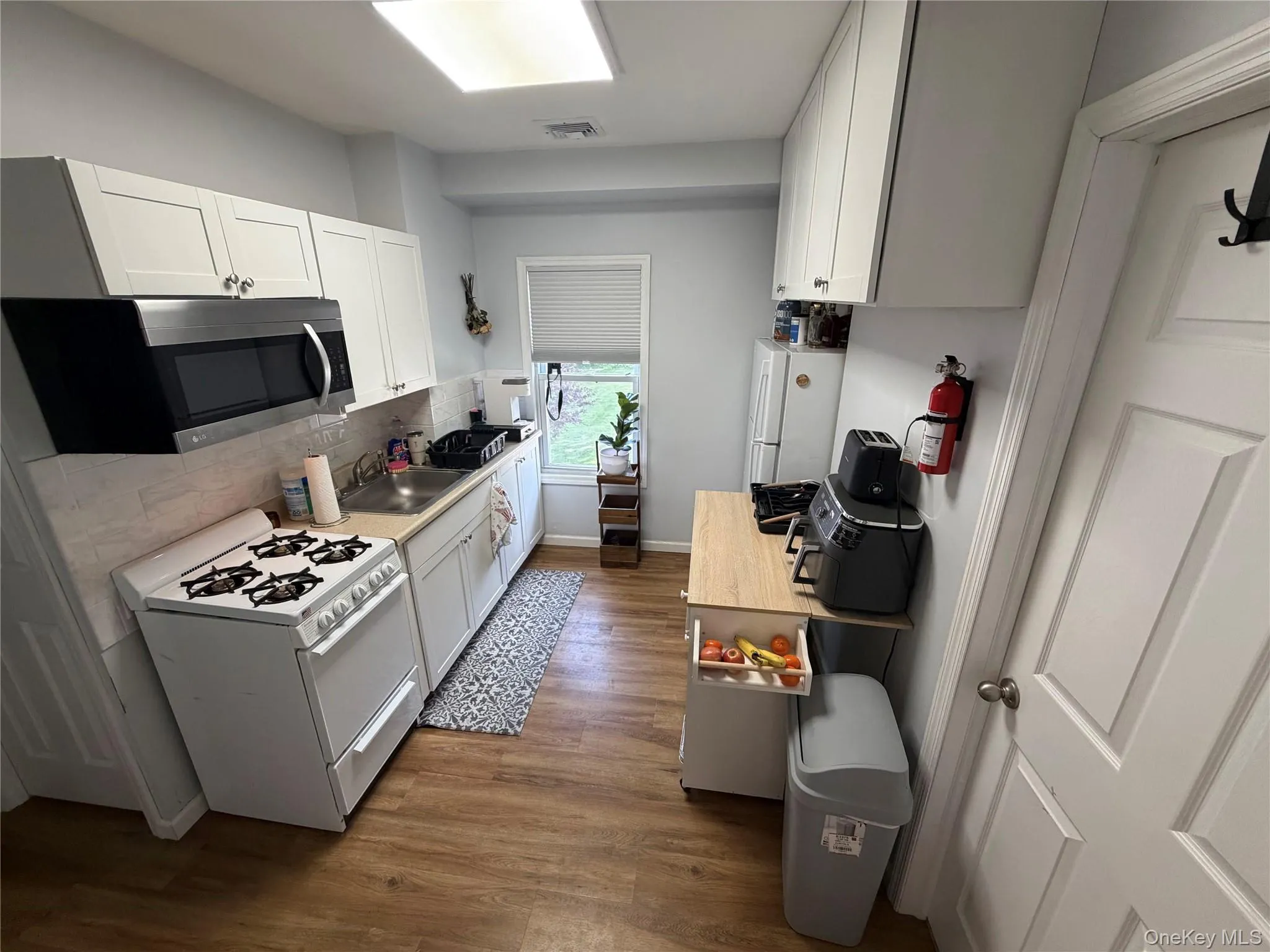 Kitchen featuring wood-finish flooring, white cabinetry, stainless steel microwave, and a window with a blind Kitchen featuring wood-finish flooring, white cabinetry, stainless steel microwave, and a window with a blind