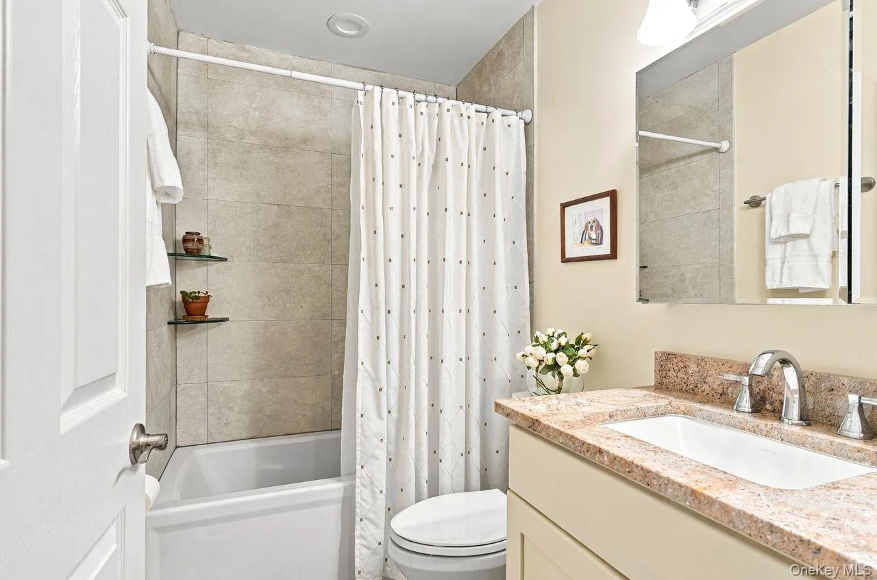 Bathroom featuring a built-in bathtub with tiled surround, a vanity with a countertop, an undermount sink, and a wall-mounted mirror Bathroom featuring a built-in bathtub with tiled surround, a vanity with a countertop, an undermount sink, and a wall-mounted mirror