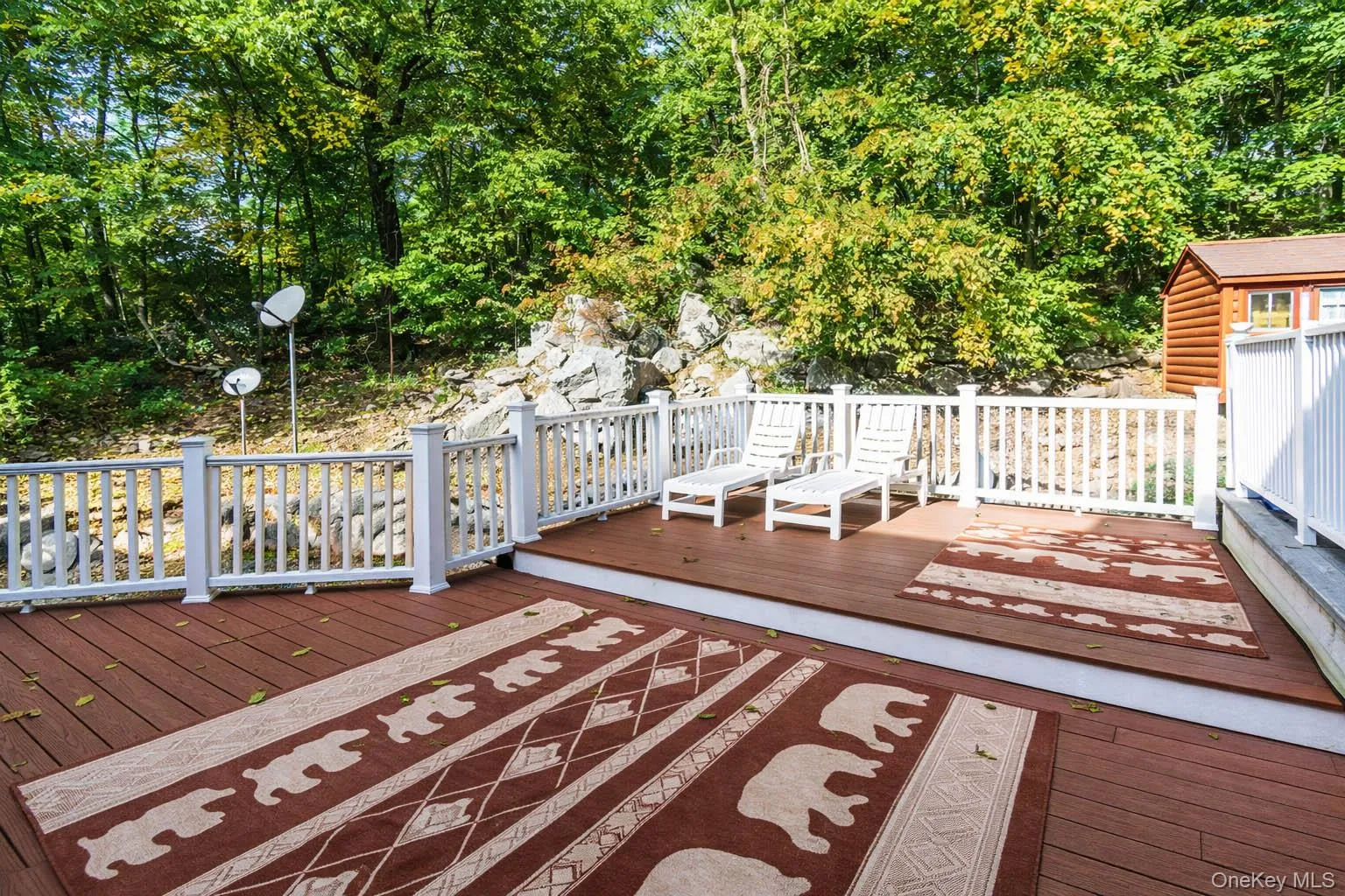 Multi-level outdoor deck with composite decking and white railing, surrounded by natural rock formations and mature trees Multi-level outdoor deck with composite decking and white railing, surrounded by natural rock formations and mature trees