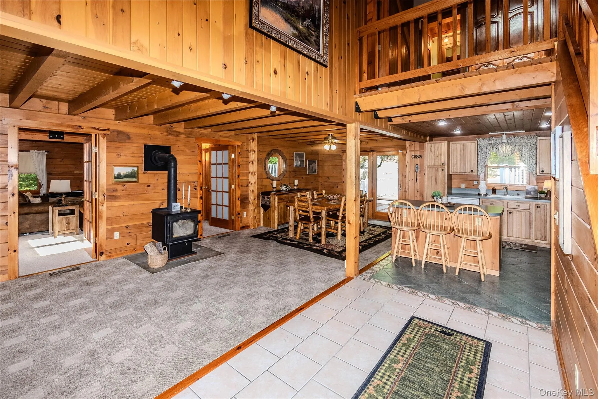 Wood-paneled interior featuring a wood-burning stove, exposed wood beam ceiling, and a kitchen with wood cabinetry Wood-paneled interior featuring a wood-burning stove, exposed wood beam ceiling, and a kitchen with wood cabinetry