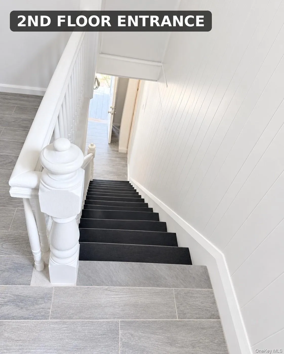 Stairway featuring a white wood banister, dark-colored stair treads, and light-toned tile flooring Stairway featuring a white wood banister, dark-colored stair treads, and light-toned tile flooring