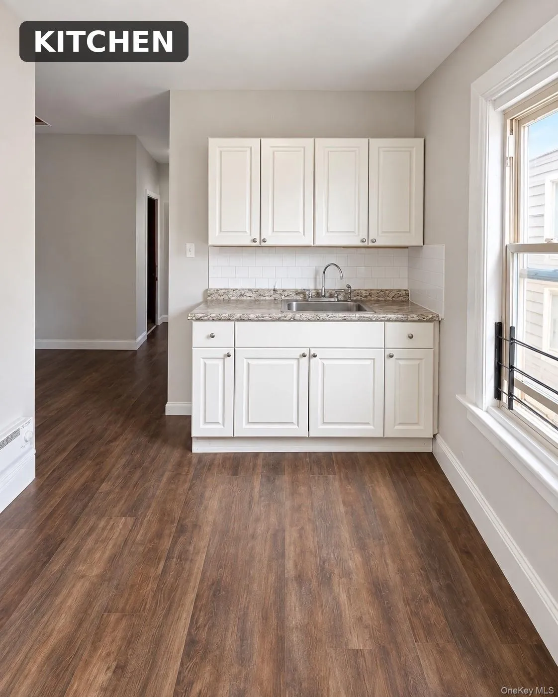 Wood-finish flooring throughout, white cabinetry, a granite-finish countertop, and a stainless steel sink with a chrome faucet Wood-finish flooring throughout, white cabinetry, a granite-finish countertop, and a stainless steel sink with a chrome faucet