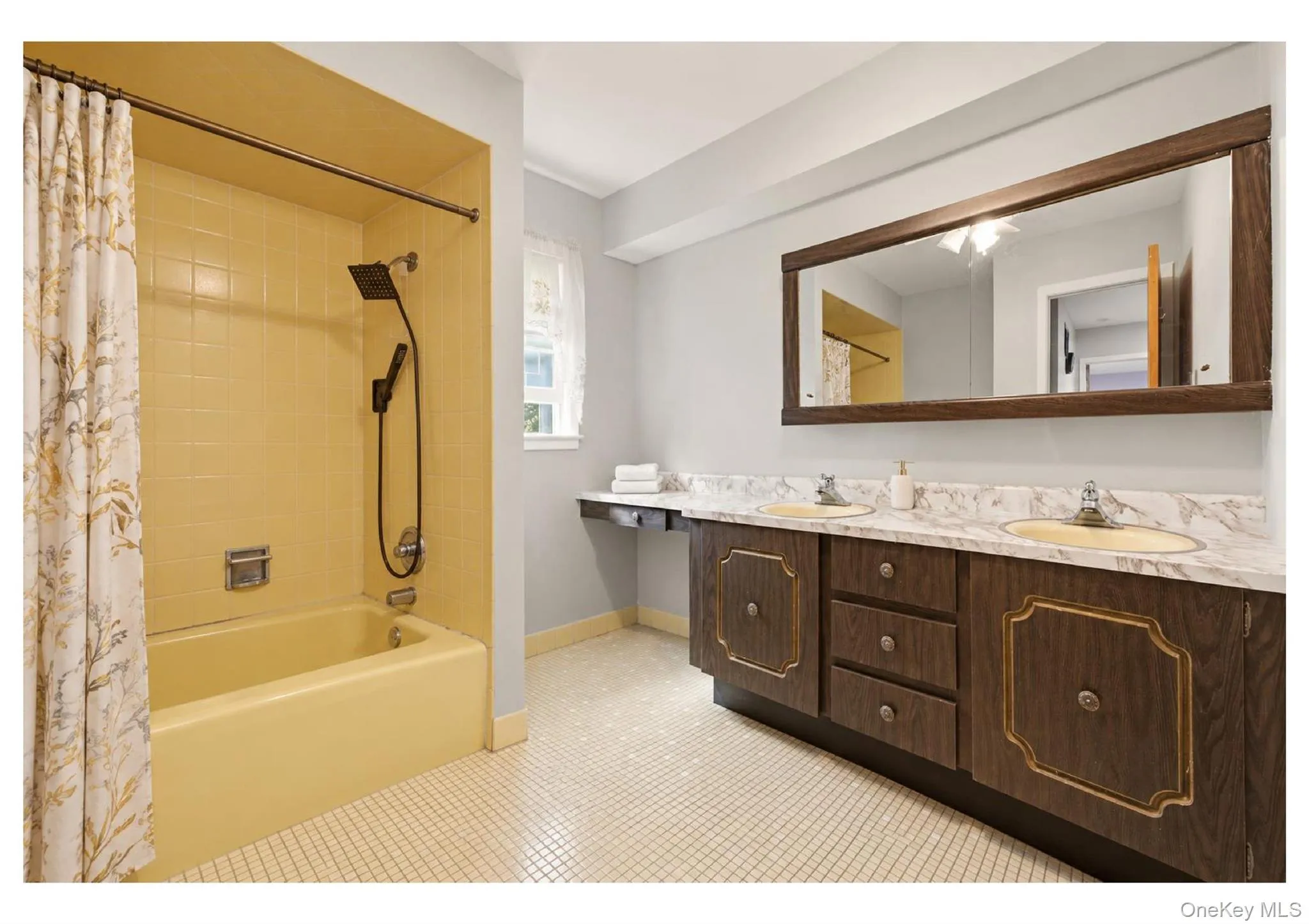 Dual-sink vanity with a marbelized countertop, wood-finish cabinetry, and a large framed mirror Dual-sink vanity with a marbelized countertop, wood-finish cabinetry, and a large framed mirror