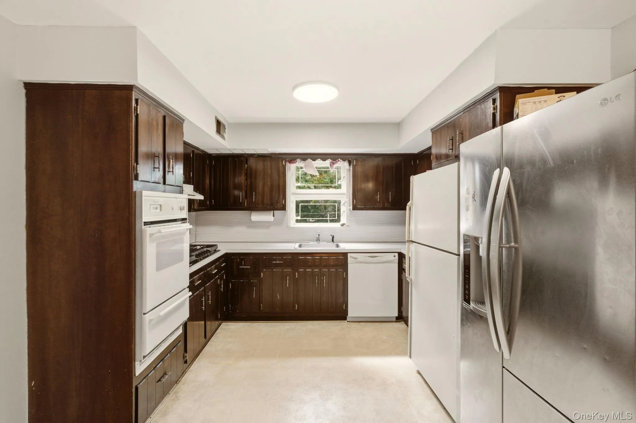 Dark wood-finish cabinetry, white countertop, built-in double oven, and a circular ceiling light fixture Dark wood-finish cabinetry, white countertop, built-in double oven, and a circular ceiling light fixture