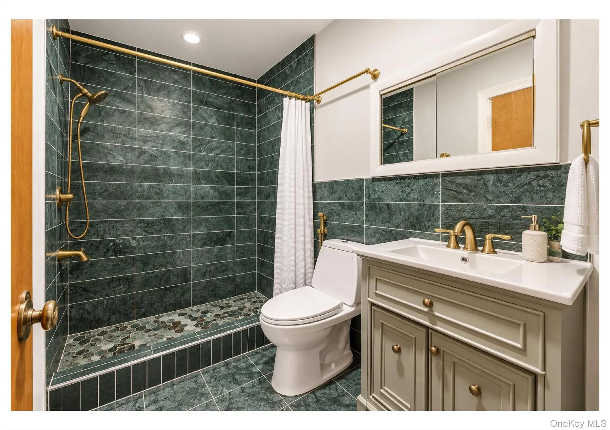 Bathroom featuring green tiled walls, coordinated tile flooring, a shower with a built-in bench, a vanity with a white countertop, and brass-finish fixtures Bathroom featuring green tiled walls, coordinated tile flooring, a shower with a built-in bench, a vanity with a white countertop, and brass-finish fixtures
