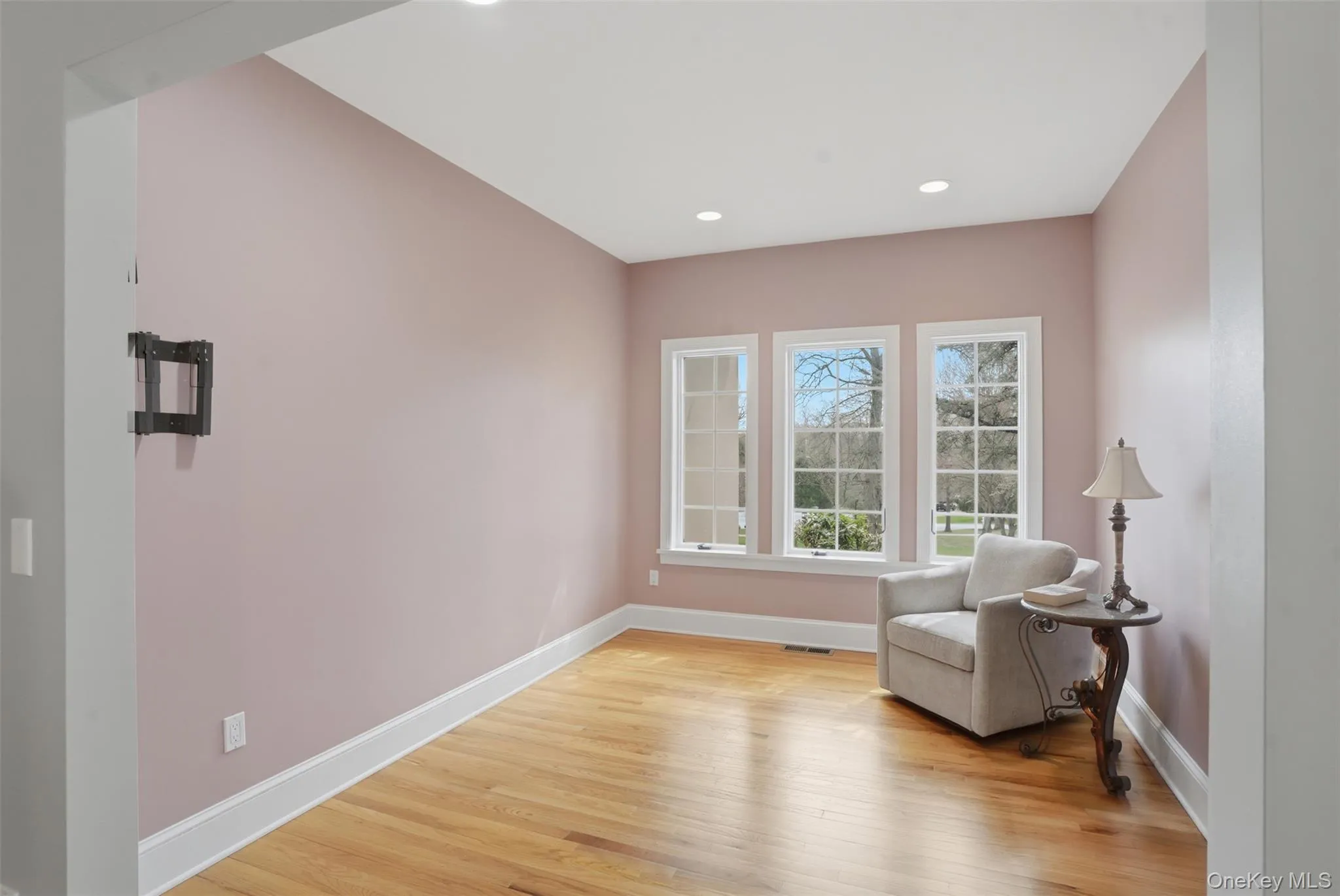 This room features hardwood floors, three windows providing natural light, and recessed ceiling lighting This room features hardwood floors, three windows providing natural light, and recessed ceiling lighting