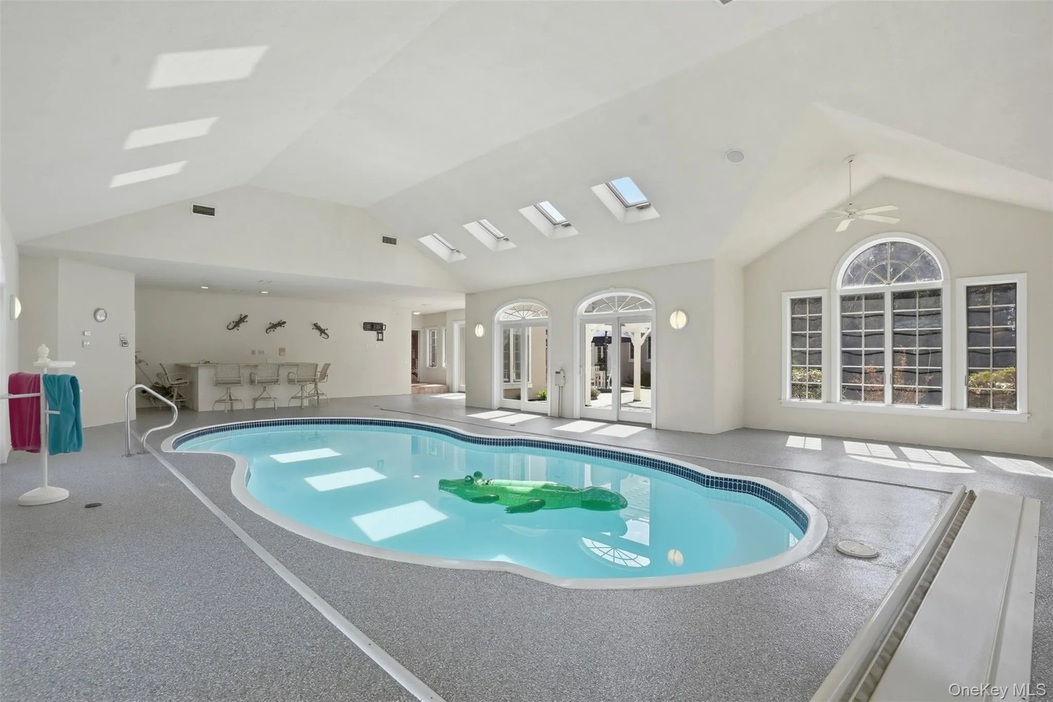 Indoor pool featuring skylights, large windows with arched transoms, and a wet bar area Indoor pool featuring skylights, large windows with arched transoms, and a wet bar area