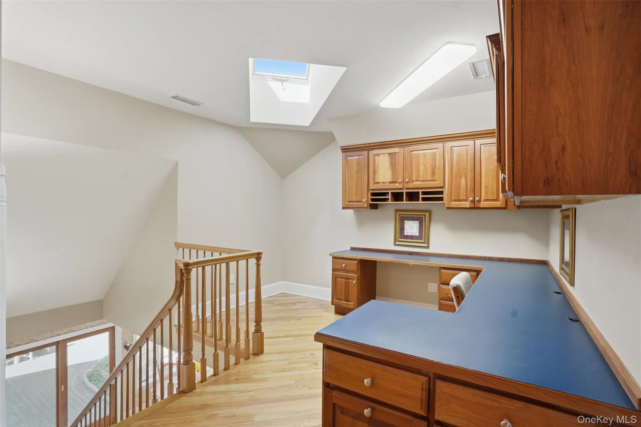 This versatile space features a built-in wooden desk and cabinetry, complemented by a skylight and hardwood flooring This versatile space features a built-in wooden desk and cabinetry, complemented by a skylight and hardwood flooring