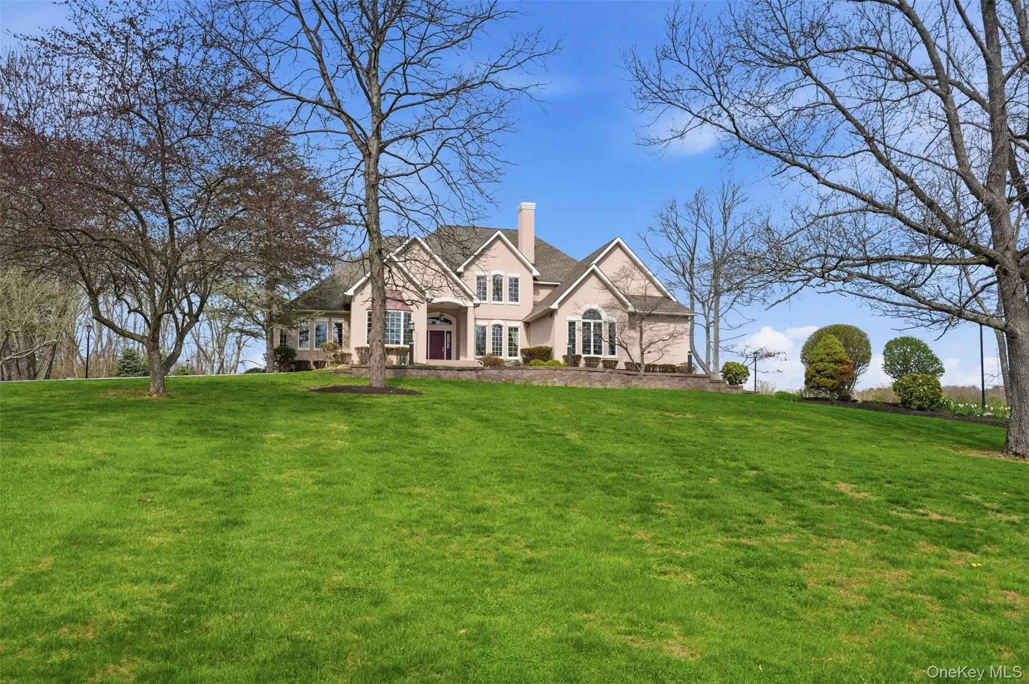 The property features a spacious front lawn with mature trees and a manicured landscape, set against a clear blue sky The property features a spacious front lawn with mature trees and a manicured landscape, set against a clear blue sky