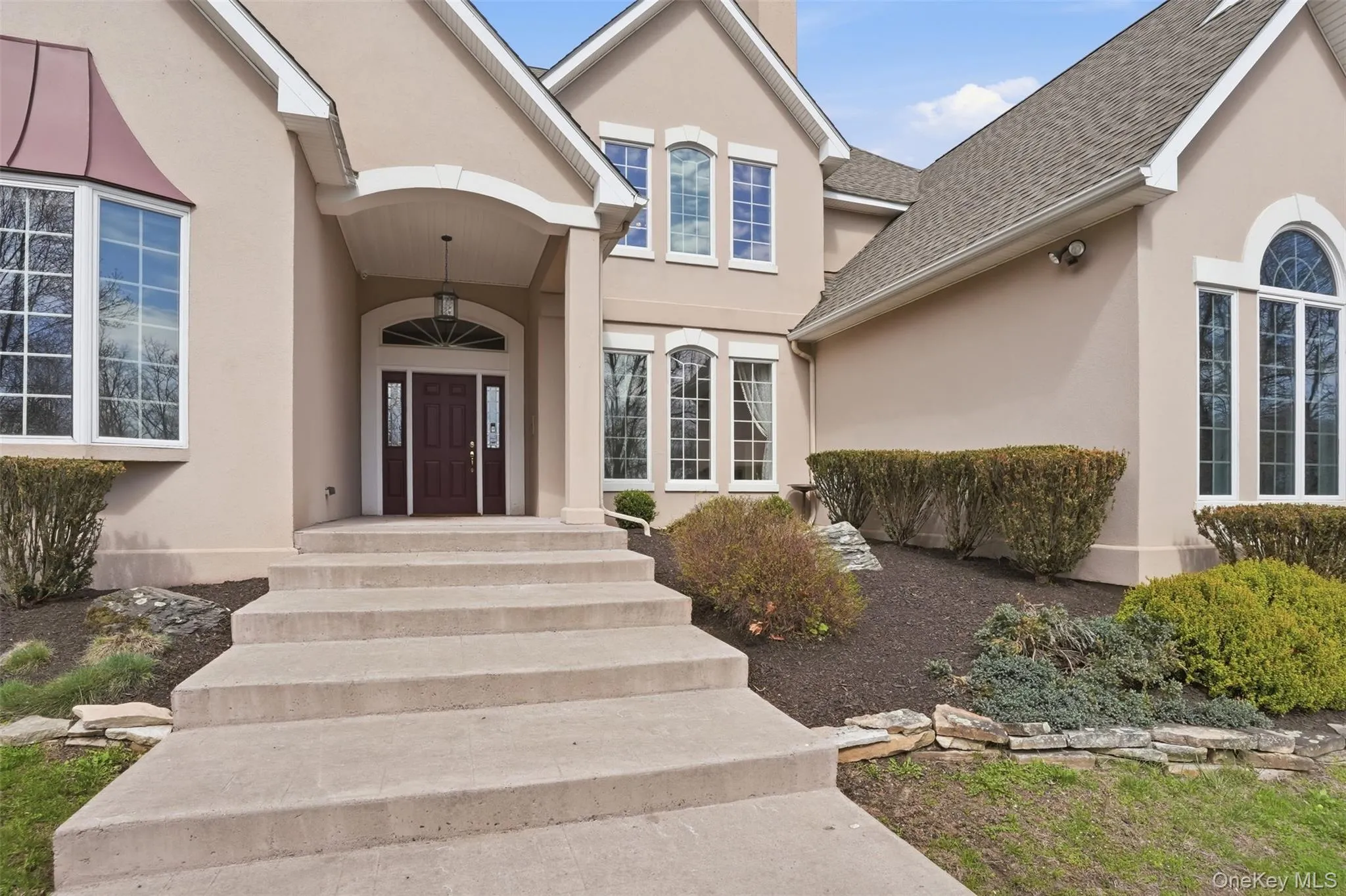 The property features a stucco exterior with a prominent covered entryway, a dark wood front door with sidelights, and arched and bay windows The property features a stucco exterior with a prominent covered entryway, a dark wood front door with sidelights, and arched and bay windows