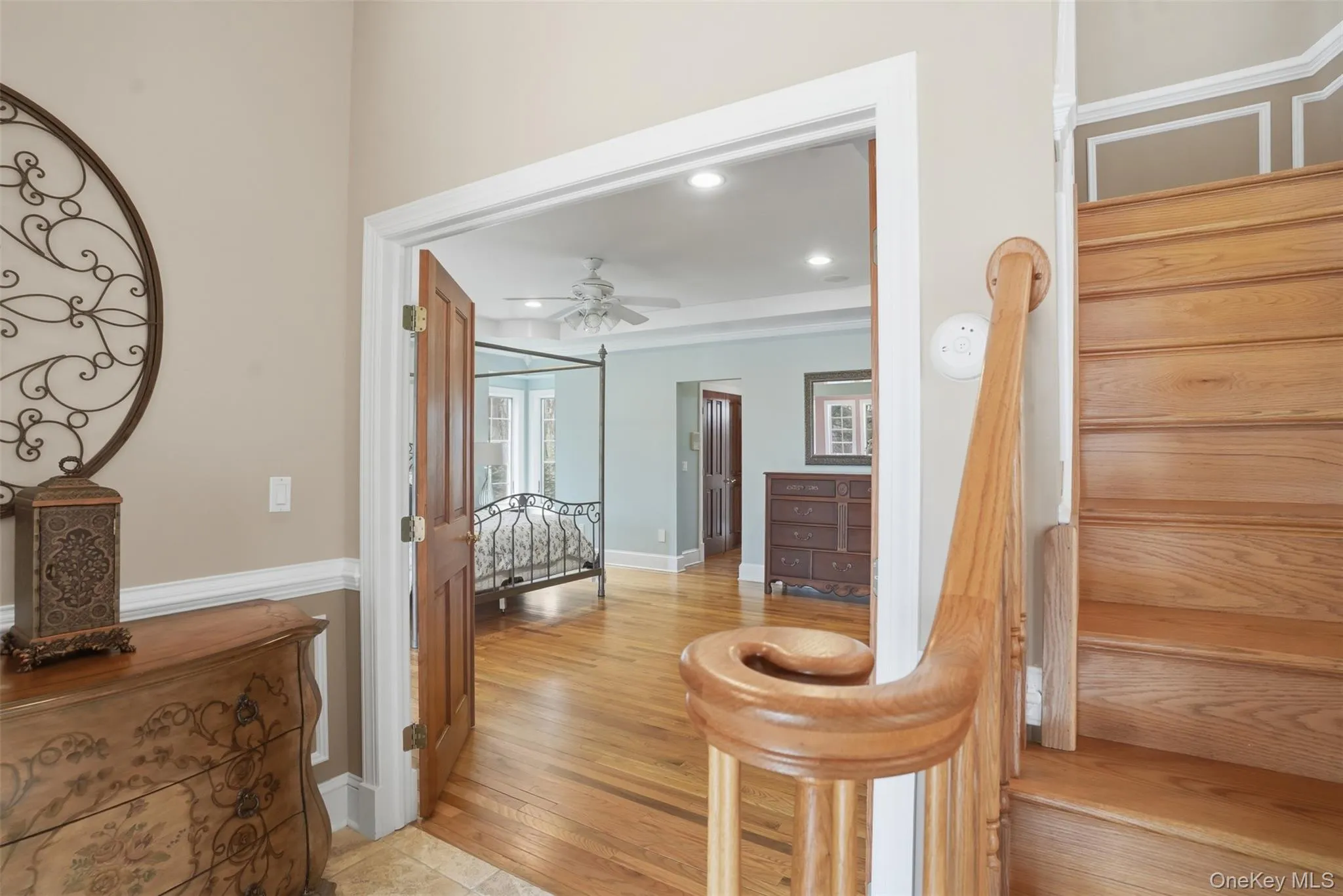 Entryway featuring a wooden staircase with a banister, wood flooring, and a doorway leading into a room with wood flooring and a ceiling fan Entryway featuring a wooden staircase with a banister, wood flooring, and a doorway leading into a room with wood flooring and a ceiling fan
