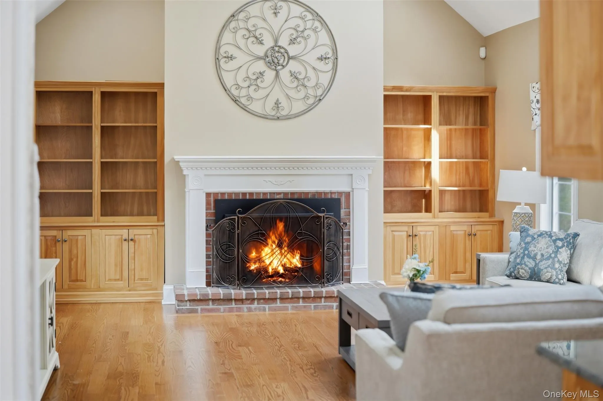 Living area featuring hardwood floors, a brick fireplace with a white mantel, and built-in wooden shelving units Living area featuring hardwood floors, a brick fireplace with a white mantel, and built-in wooden shelving units
