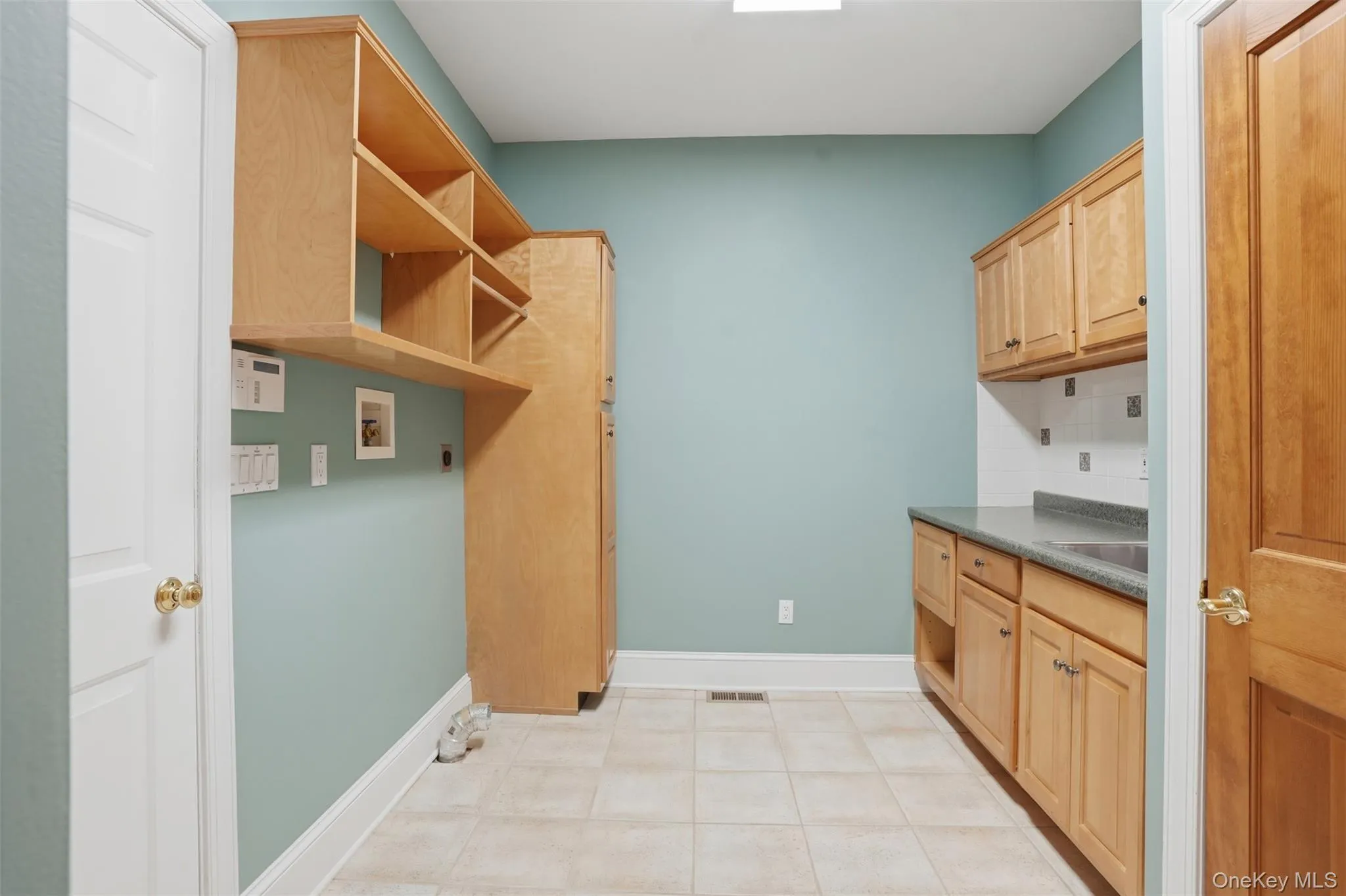 Utility room with light wood cabinetry, shelving, a countertop, and tiled flooring Utility room with light wood cabinetry, shelving, a countertop, and tiled flooring