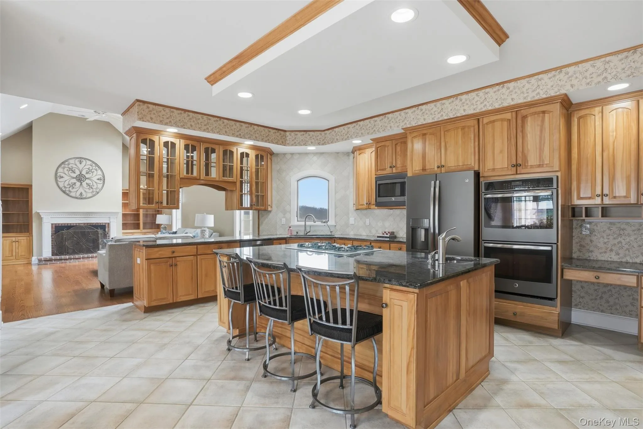 Spacious kitchen featuring extensive cabinetry, an island with a dark countertop, a stainless steel refrigerator, and integrated double ovens Spacious kitchen featuring extensive cabinetry, an island with a dark countertop, a stainless steel refrigerator, and integrated double ovens