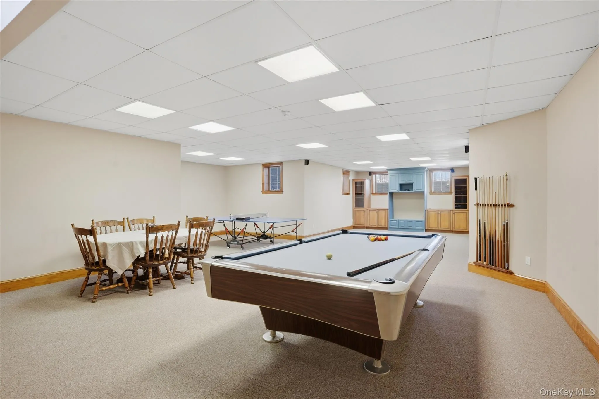 Spacious recreation room featuring carpeted flooring, recessed lighting, and a built-in entertainment area with light blue and natural wood cabinetry Spacious recreation room featuring carpeted flooring, recessed lighting, and a built-in entertainment area with light blue and natural wood cabinetry