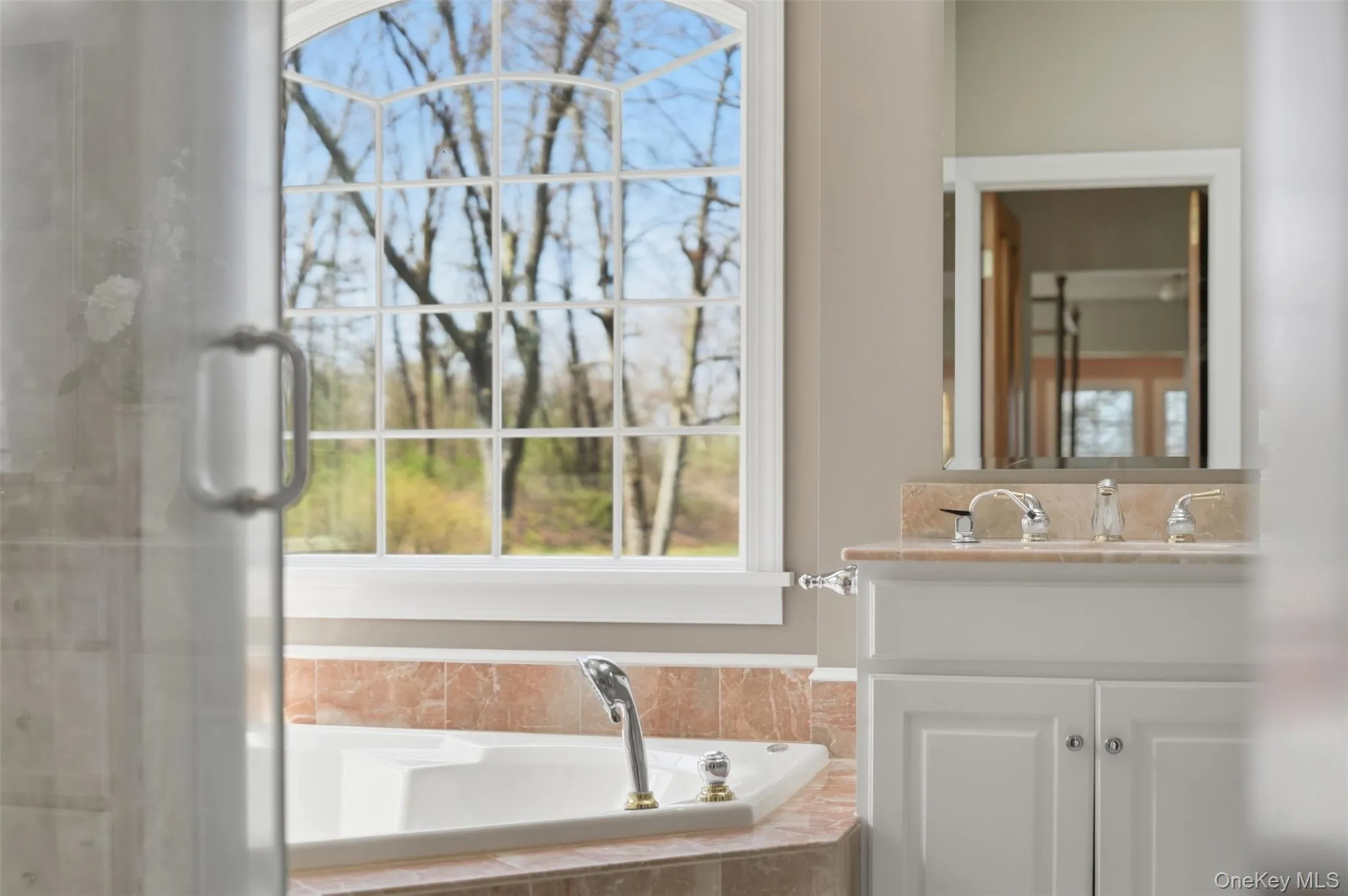 Bathroom featuring a built-in tub with a tiled surround, a large arched window, and a vanity with a light-colored countertop Bathroom featuring a built-in tub with a tiled surround, a large arched window, and a vanity with a light-colored countertop