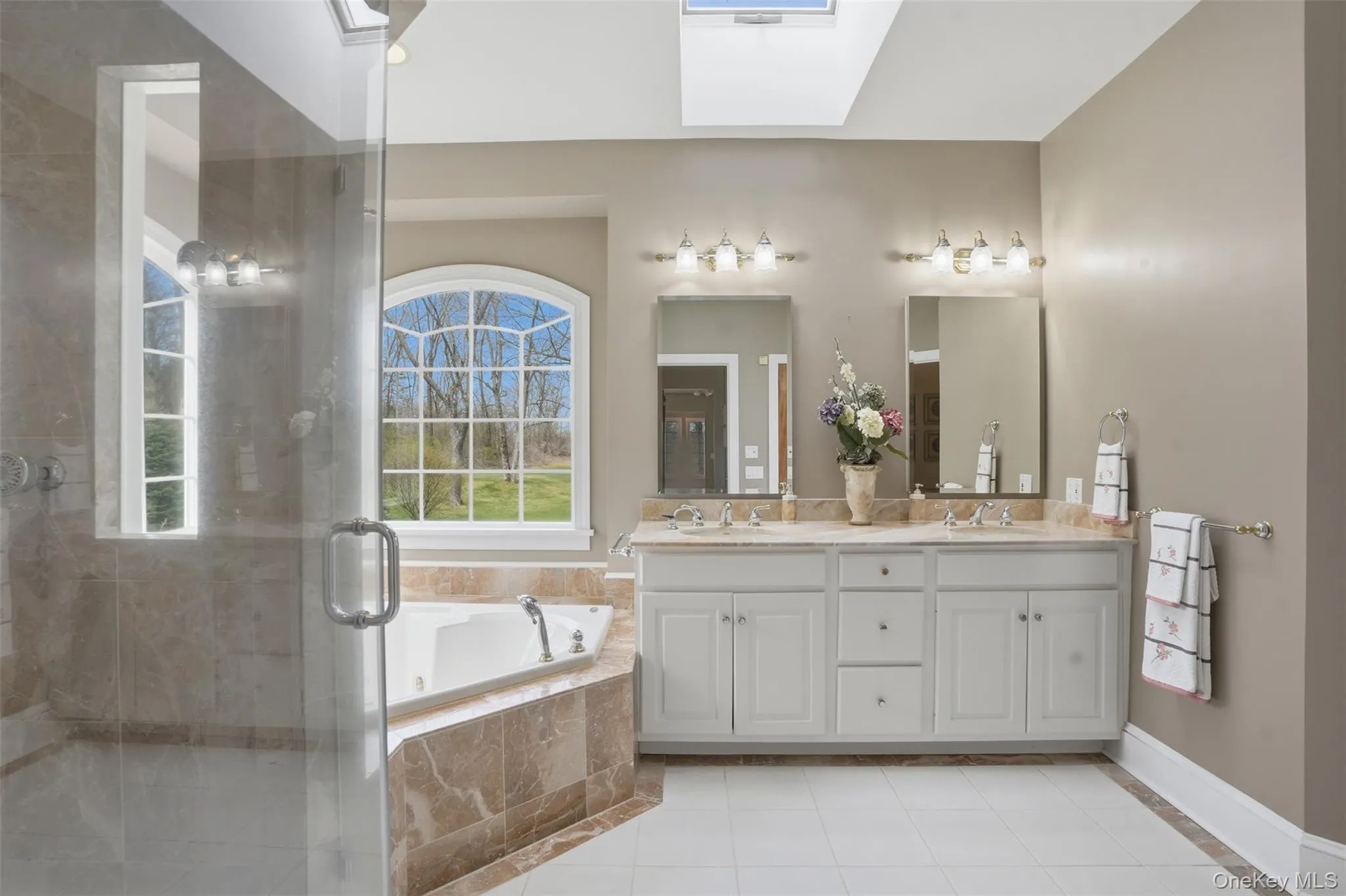 The bathroom features a spacious shower with a glass enclosure, a corner bathtub, and a dual vanity with two mirrors and overhead lighting The bathroom features a spacious shower with a glass enclosure, a corner bathtub, and a dual vanity with two mirrors and overhead lighting