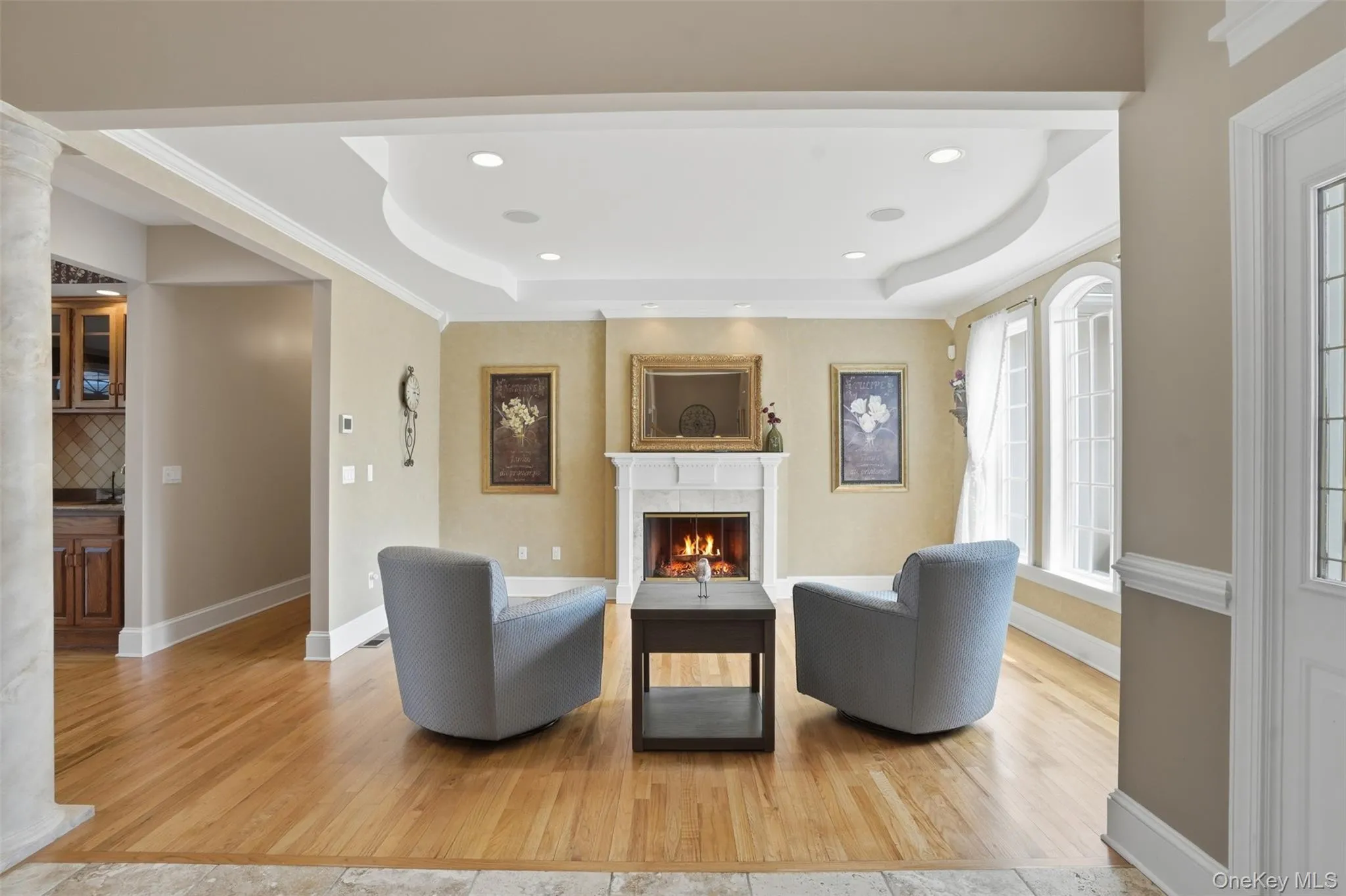 Living area featuring hardwood floors, a fireplace with a white mantel, recessed lighting, and large windows providing natural light Living area featuring hardwood floors, a fireplace with a white mantel, recessed lighting, and large windows providing natural light
