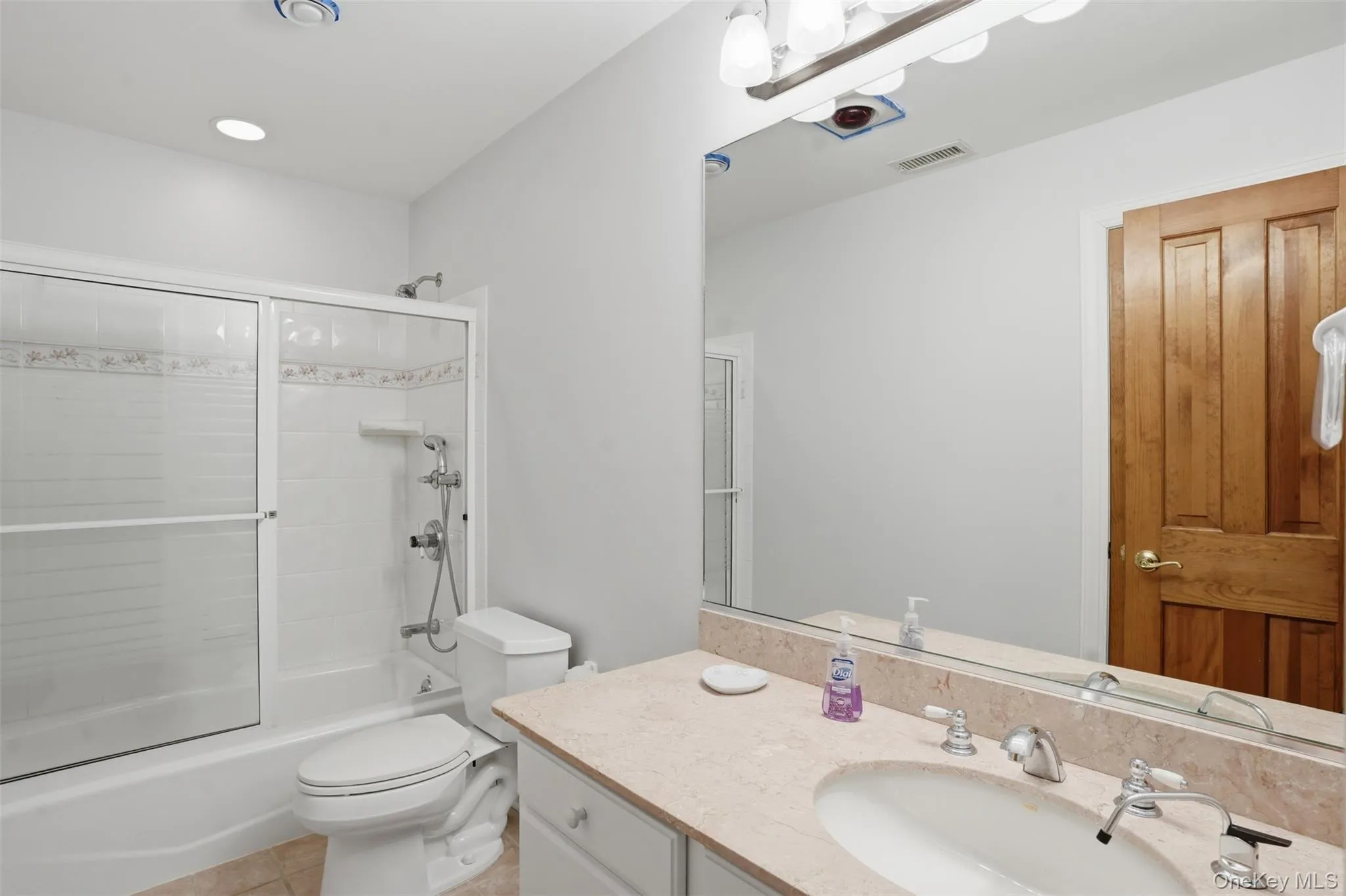 The bathroom features a vanity with a light-colored countertop and a mirror, and a shower-tub combination with sliding glass doors The bathroom features a vanity with a light-colored countertop and a mirror, and a shower-tub combination with sliding glass doors