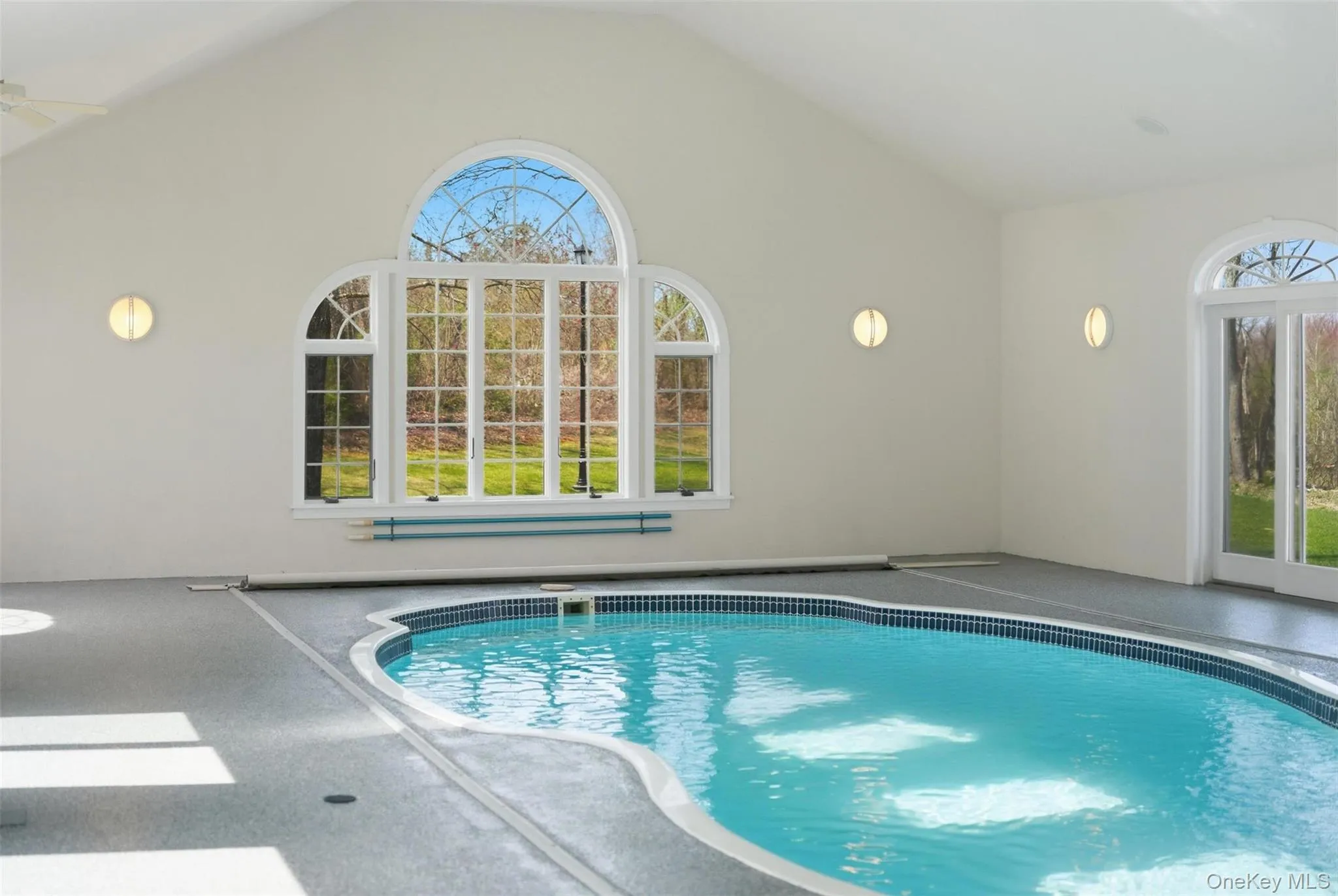 Indoor pool area featuring an arched window, a tiled pool with a blue interior, and access to the outdoors via French doors Indoor pool area featuring an arched window, a tiled pool with a blue interior, and access to the outdoors via French doors