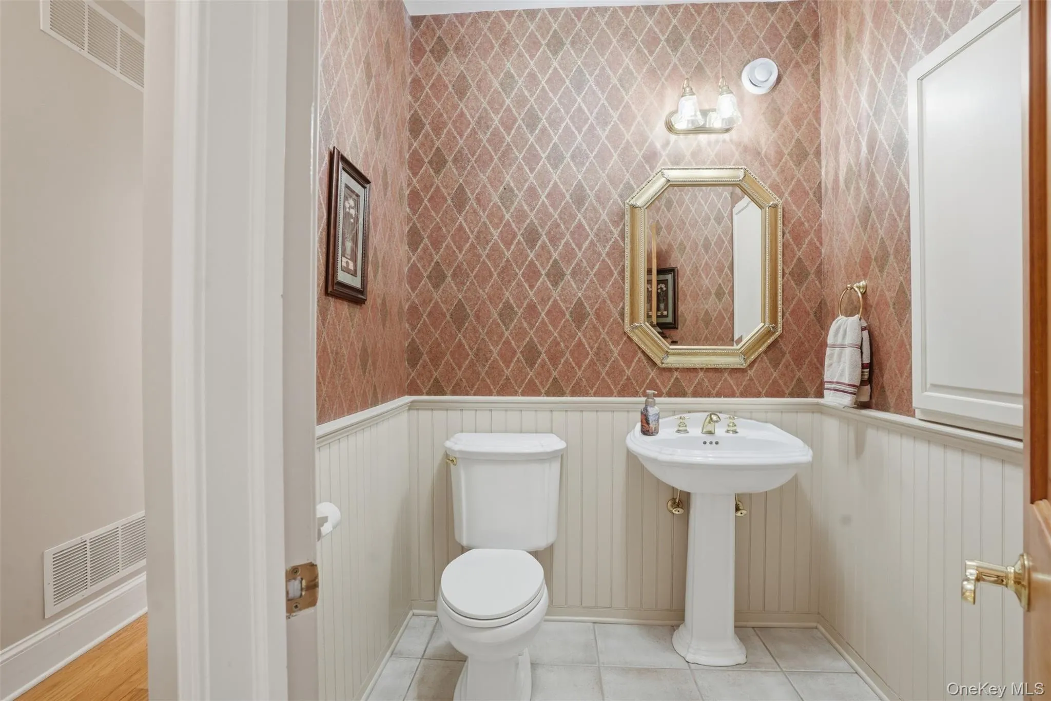 The powder room features a pedestal sink, white toilet, and patterned wallpaper above wainscoting The powder room features a pedestal sink, white toilet, and patterned wallpaper above wainscoting