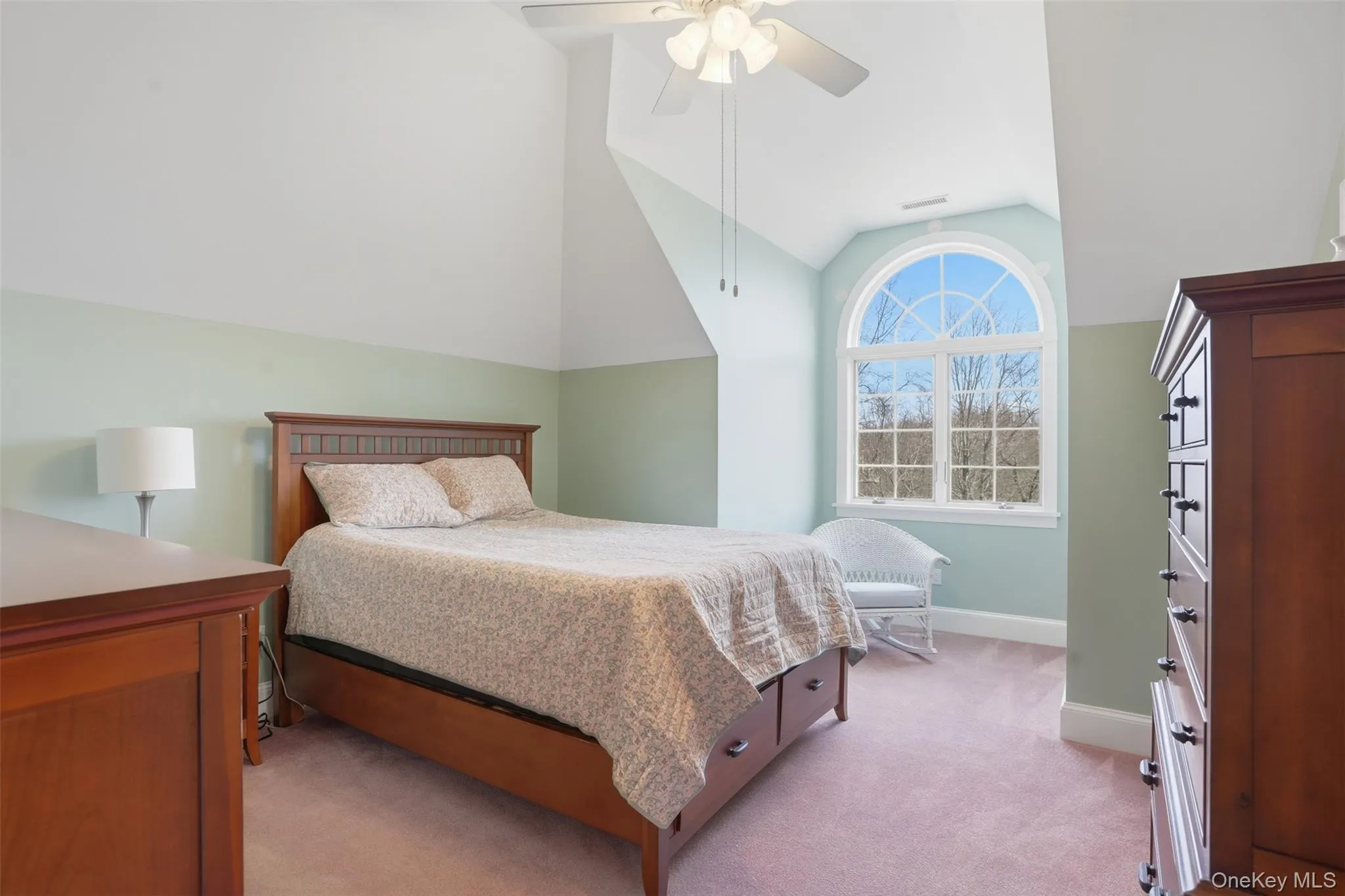 This room features an arched window with a wooded view, a sloped ceiling, and a ceiling fan This room features an arched window with a wooded view, a sloped ceiling, and a ceiling fan