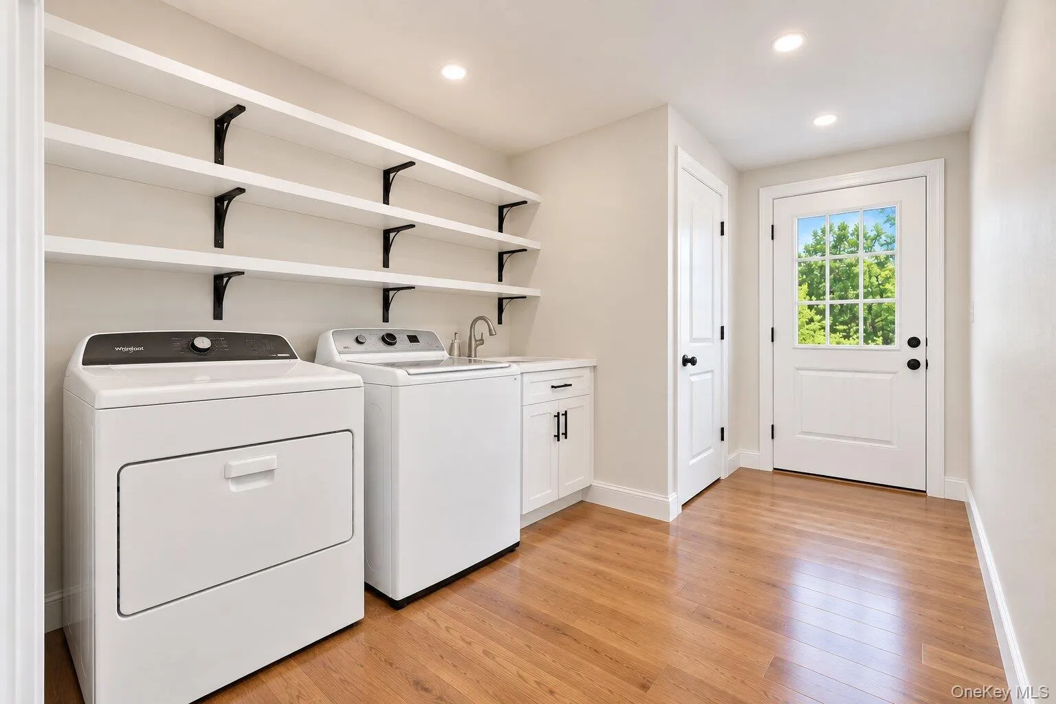 Hardwood-finish flooring, built-in shelving, white cabinetry with black hardware, recessed lighting, and a paneled door with a clear glass insert Hardwood-finish flooring, built-in shelving, white cabinetry with black hardware, recessed lighting, and a paneled door with a clear glass insert