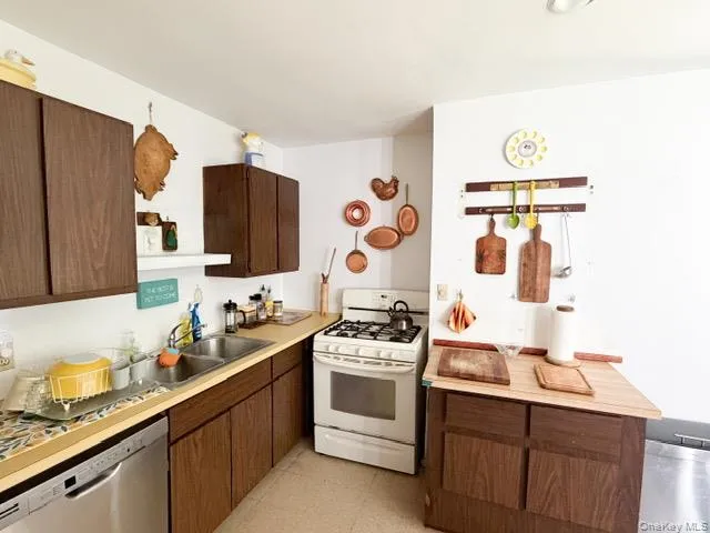 Kitchen featuring wood-finish cabinetry, a stainless steel double basin sink, and a white gas range Kitchen featuring wood-finish cabinetry, a stainless steel double basin sink, and a white gas range