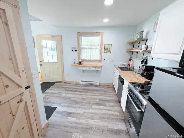 Wood-finish flooring throughout, stainless steel gas range, wooden open shelving, light wood countertops, and a full-light panel door Wood-finish flooring throughout, stainless steel gas range, wooden open shelving, light wood countertops, and a full-light panel door