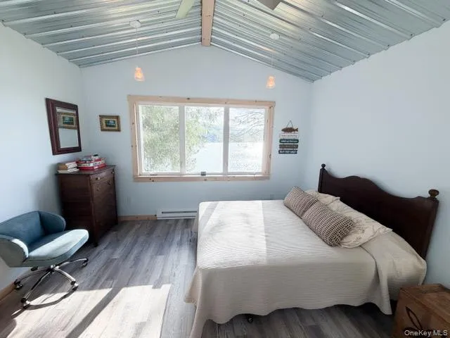Vaulted metal ceiling with exposed wood beams, large window with wood trim, and wood-finish flooring Vaulted metal ceiling with exposed wood beams, large window with wood trim, and wood-finish flooring