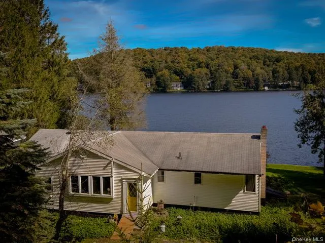 Lakefront property with mature trees, a shingled roof, and a prominent chimney Lakefront property with mature trees, a shingled roof, and a prominent chimney