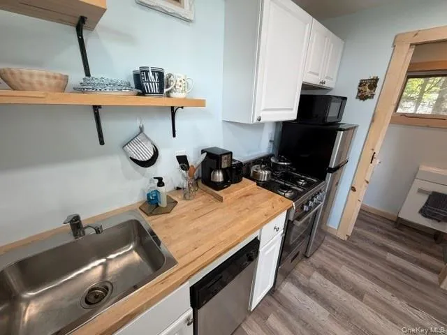 Kitchen featuring wood-finish countertops, stainless steel sink, white cabinetry, stainless steel dishwasher, and a gas range Kitchen featuring wood-finish countertops, stainless steel sink, white cabinetry, stainless steel dishwasher, and a gas range