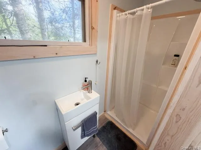 Compact bathroom featuring a white vanity with integrated sink, chrome faucet, and a stand-up shower with a white enclosure Compact bathroom featuring a white vanity with integrated sink, chrome faucet, and a stand-up shower with a white enclosure