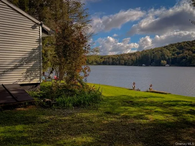 Lakeside property featuring a spacious lawn, mature trees, and a distant forested hillside Lakeside property featuring a spacious lawn, mature trees, and a distant forested hillside