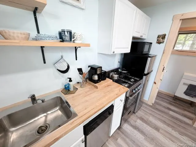 Compact kitchen featuring wood-finish countertops, a stainless steel sink, a dishwasher, a freestanding range, and upper cabinetry Compact kitchen featuring wood-finish countertops, a stainless steel sink, a dishwasher, a freestanding range, and upper cabinetry