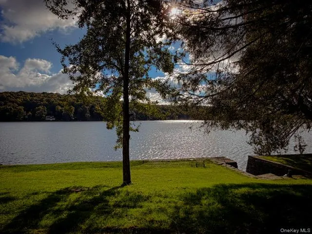 Expansive waterfront property featuring a manicured lawn, mature trees, and a stone retaining wall Expansive waterfront property featuring a manicured lawn, mature trees, and a stone retaining wall