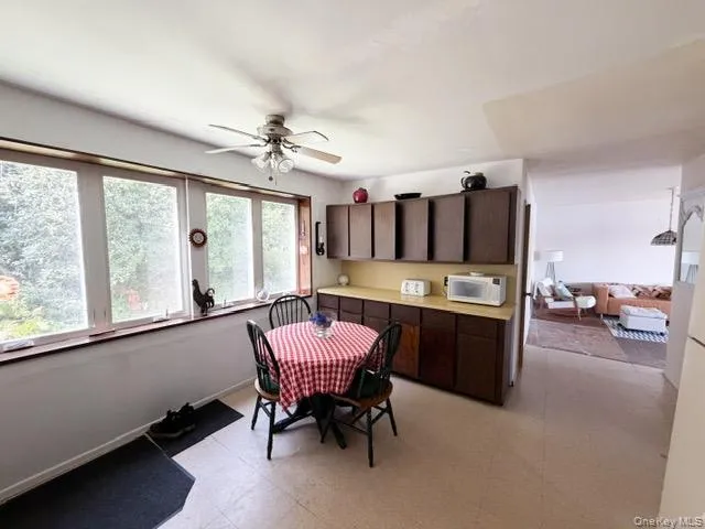 Kitchen area featuring a ceiling fan with integrated lighting, wood-finish cabinetry, a light-toned countertop, and expansive windows Kitchen area featuring a ceiling fan with integrated lighting, wood-finish cabinetry, a light-toned countertop, and expansive windows