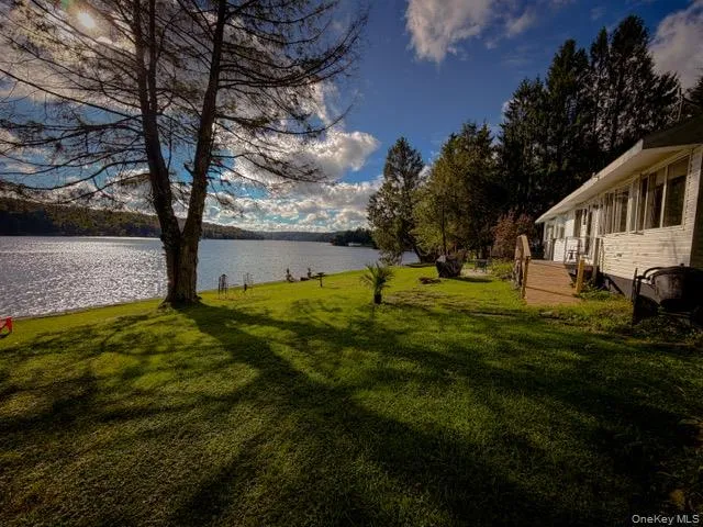 Lakefront property with a white exterior, a wood-finish deck, and mature trees Lakefront property with a white exterior, a wood-finish deck, and mature trees