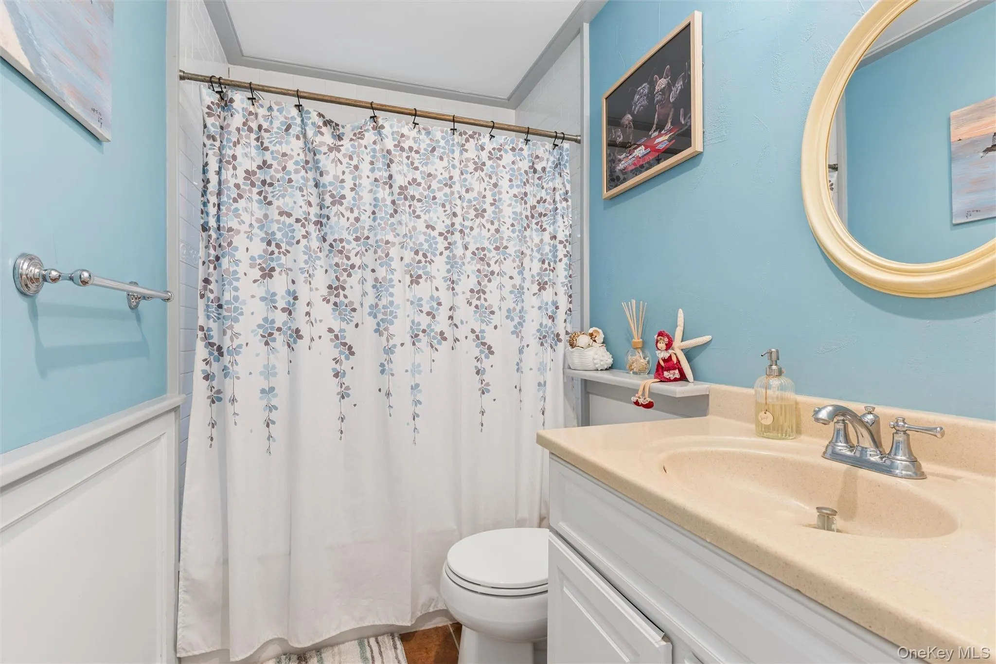 White paneled wainscoting with a light blue wall, a built-in vanity with a single basin, and a wall-mounted oval mirror White paneled wainscoting with a light blue wall, a built-in vanity with a single basin, and a wall-mounted oval mirror