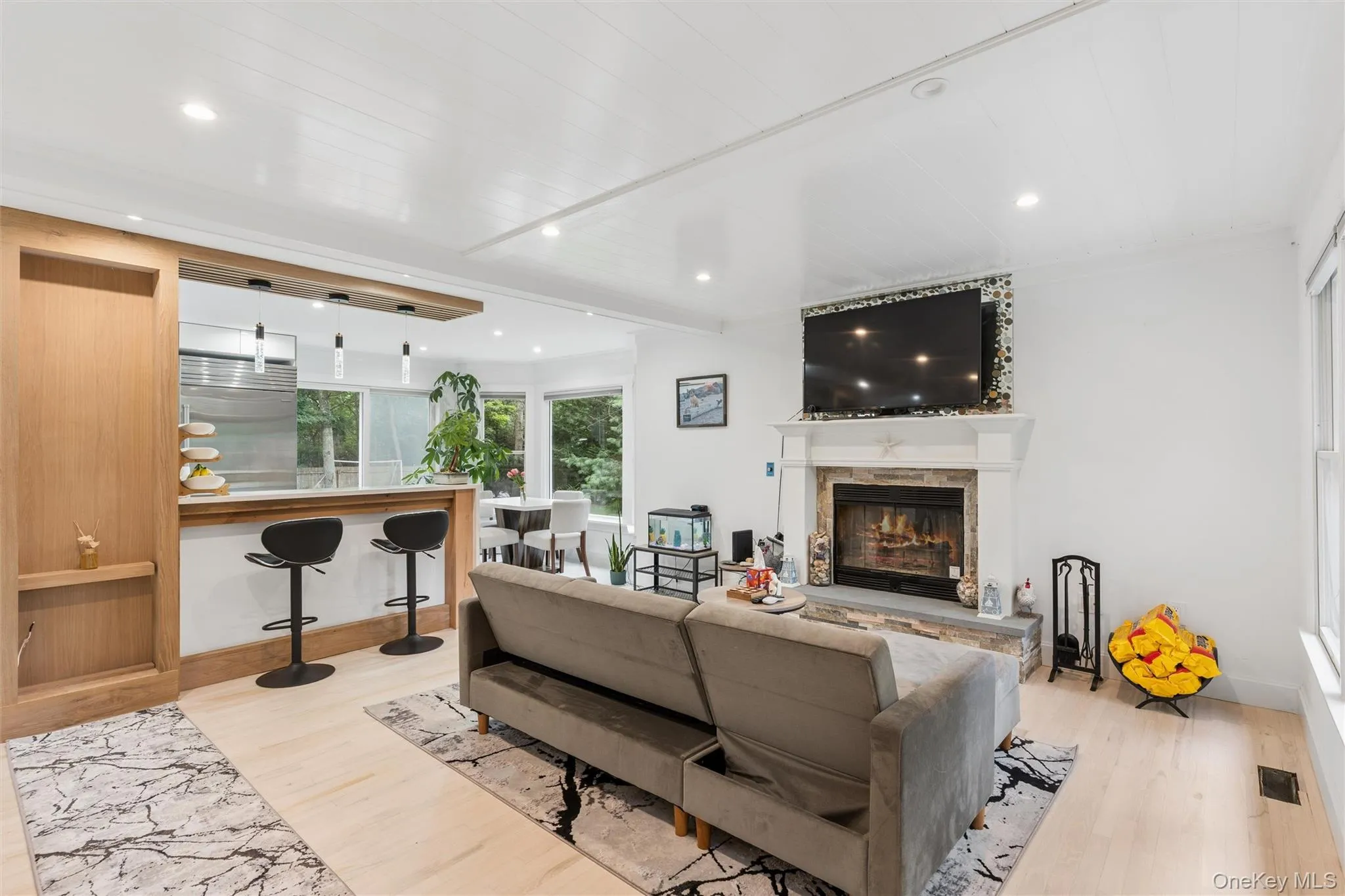Open-concept living area featuring a stone-clad fireplace, light wood-finish flooring, recessed lighting, and a white shiplap ceiling Open-concept living area featuring a stone-clad fireplace, light wood-finish flooring, recessed lighting, and a white shiplap ceiling