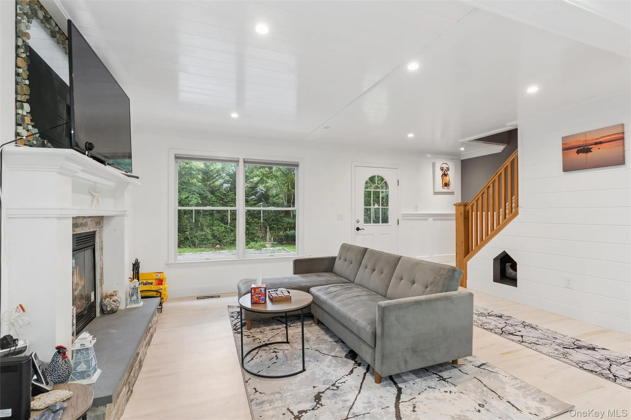 Recessed lighting, wood-finish flooring, a white-painted fireplace with a stone hearth, a multi-pane entry door, and a natural wood staircase with a built-in alcove Recessed lighting, wood-finish flooring, a white-painted fireplace with a stone hearth, a multi-pane entry door, and a natural wood staircase with a built-in alcove